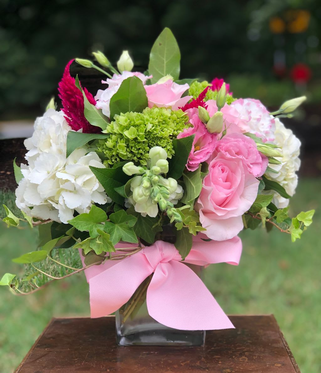 Pink and white flower bouquet in a square glass vase with a pink ribbon