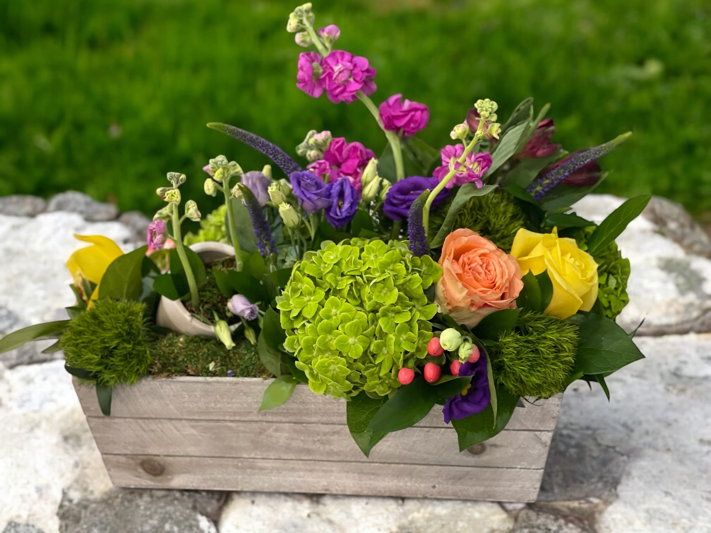 Mixed floral arrangement in a wooden box with bright pink, purple, yellow, and peach blooms
