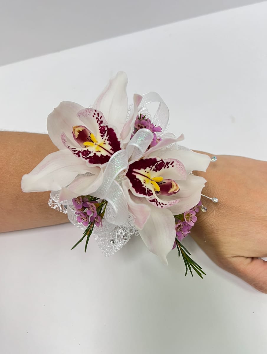 Wrist corsage with two white orchids, pink accents, and white ribbon on an arm