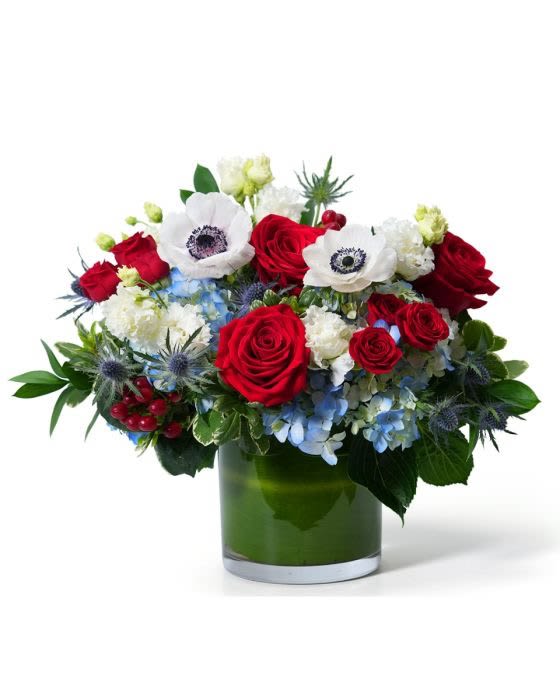Red, white, and blue flower arrangement with roses and anemones in a green-lined glass cylinder vase