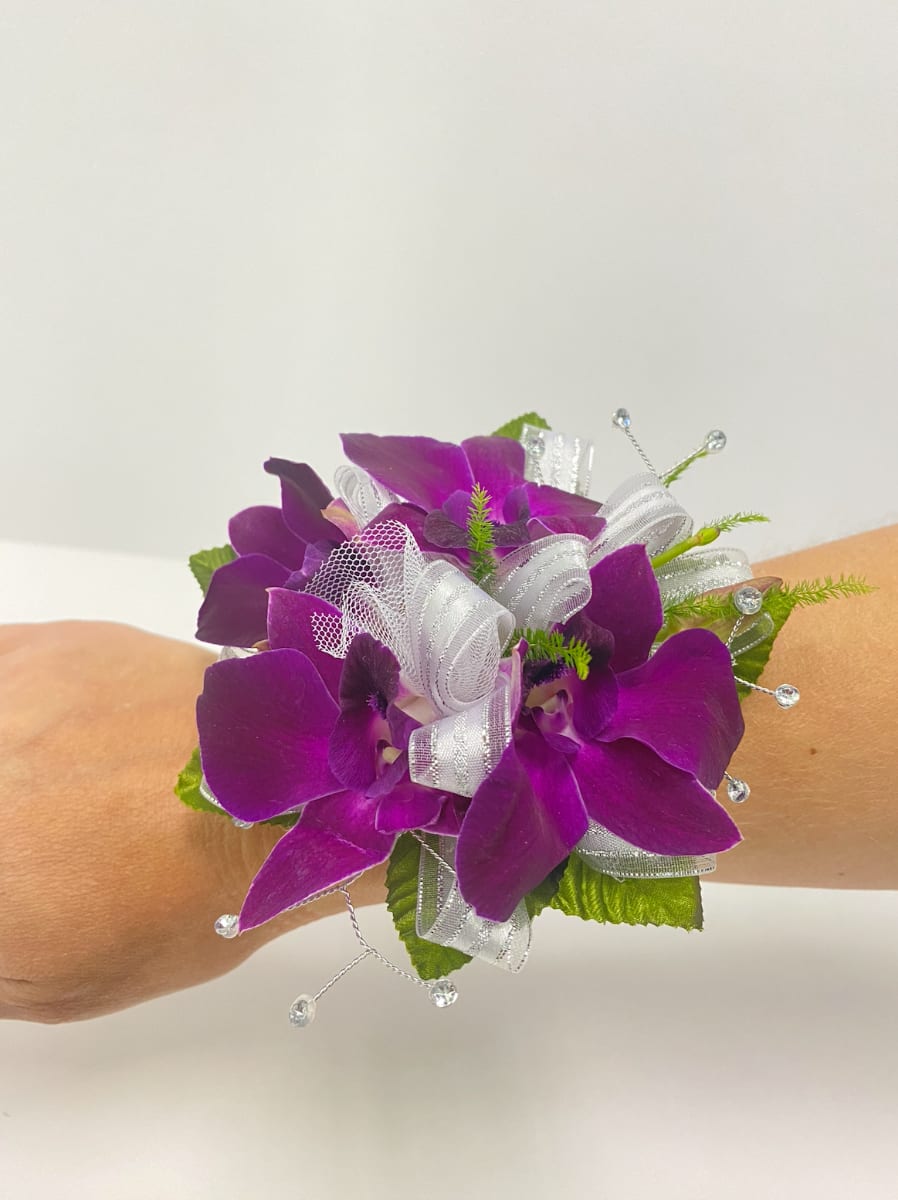 Purple orchid wrist corsage with white ribbon and beads worn on an arm