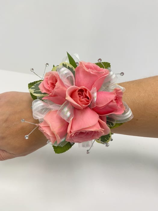 Pink rose wrist corsage with white ribbon accents and crystal bead sprays on a person's arm