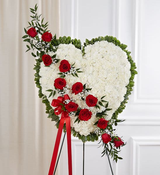 Heart-shaped white floral standing wreath with red roses on an easel.