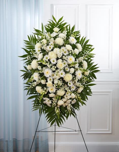Standing spray of white roses, daisies, and mums with palm fronds on a metal easel.