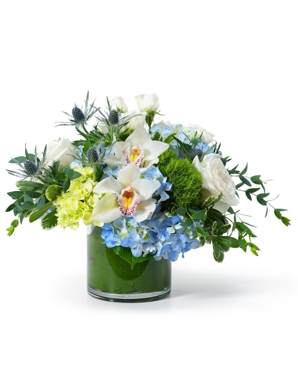 Low glass vase arrangement with blue hydrangeas, white roses, orchids, and green accents