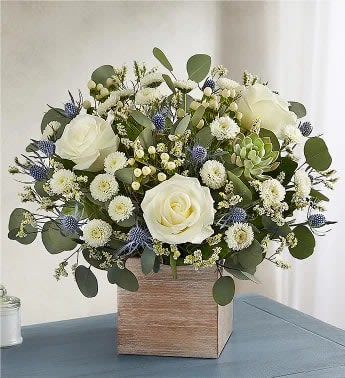 Compact arrangement of white roses and button flowers with blue accents in a wooden cube vase
