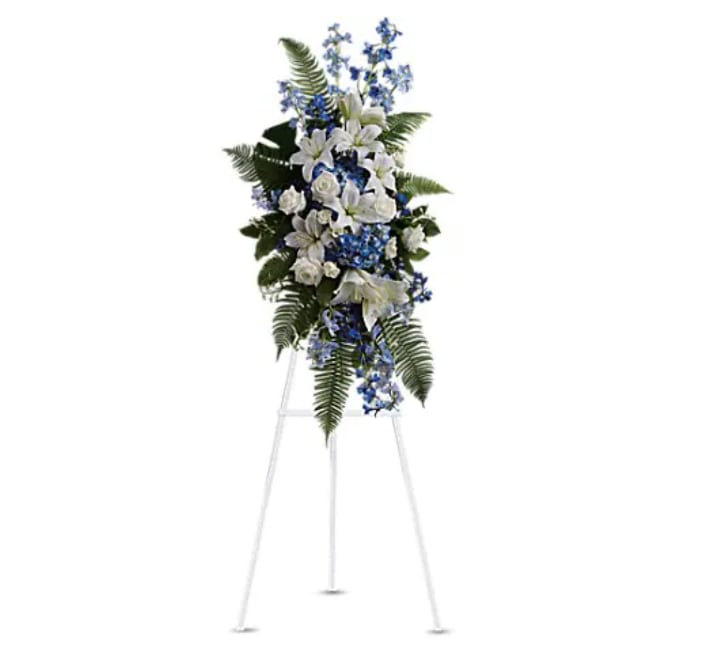 Standing floral spray with white lilies and blue flowers on an easel