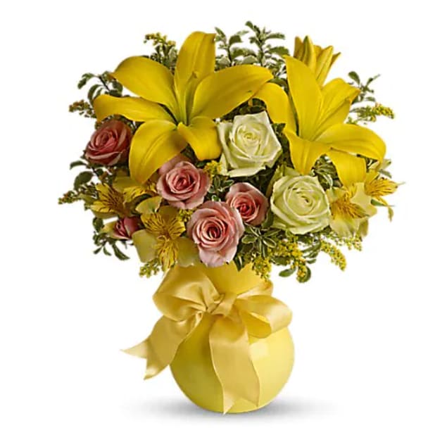 Yellow lilies and roses arranged in a gold vase with a ribbon bow