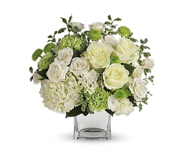 White roses and green pompons in a clear square vase