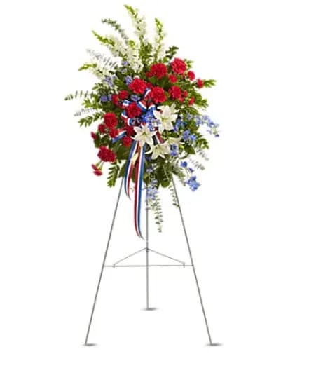 Sacred Duty Spray - Standing tall, proud and patriotic, this dazzling free-standing spray is like a fireworks display made of graceful flowers. Uniquely beautiful, it's a lovely way to honor a great loss. A gorgeous selection of flowers such as white lilies and snapdragons, blue delphinium, red carnations and miniature carnations, eucalyptus and more create this all-American spray. 
