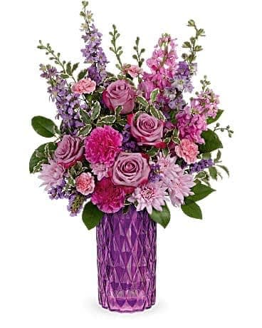 Tall arrangement of pink and purple roses, carnations, and mums in a faceted purple glass vase