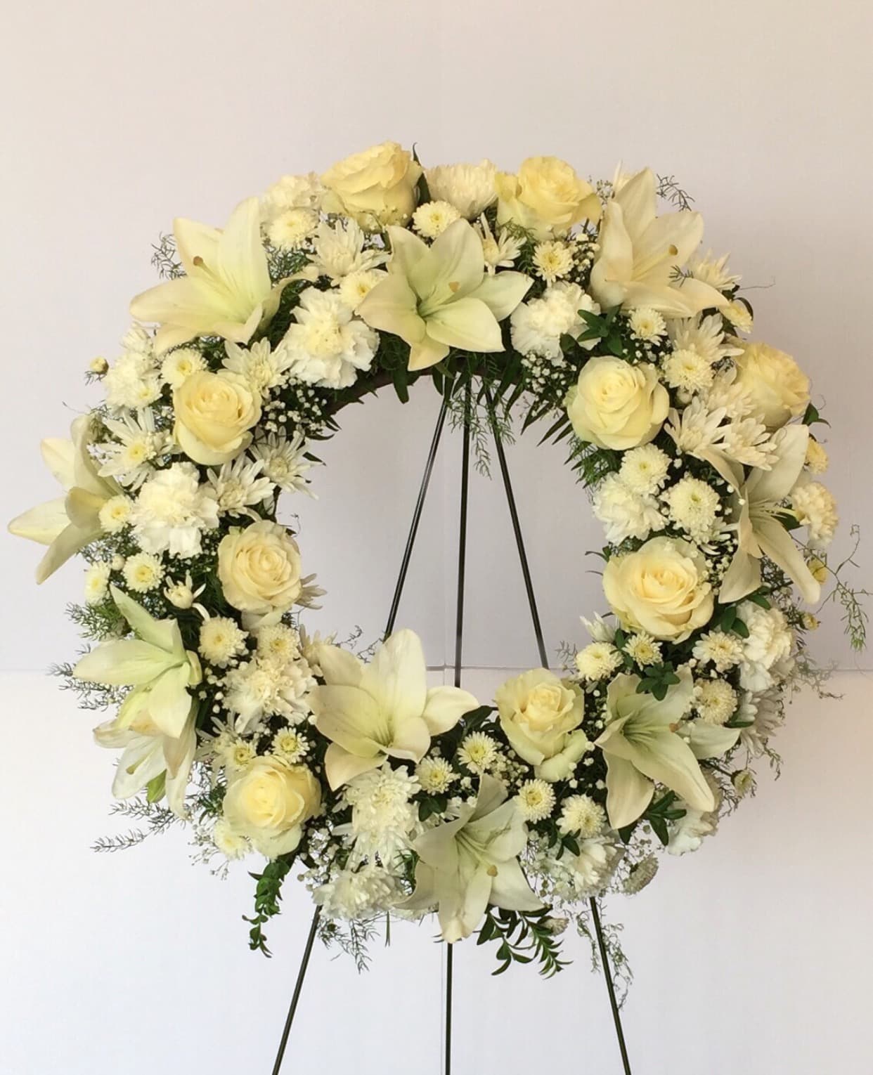 Cream floral wreath on a black stand with roses and lilies