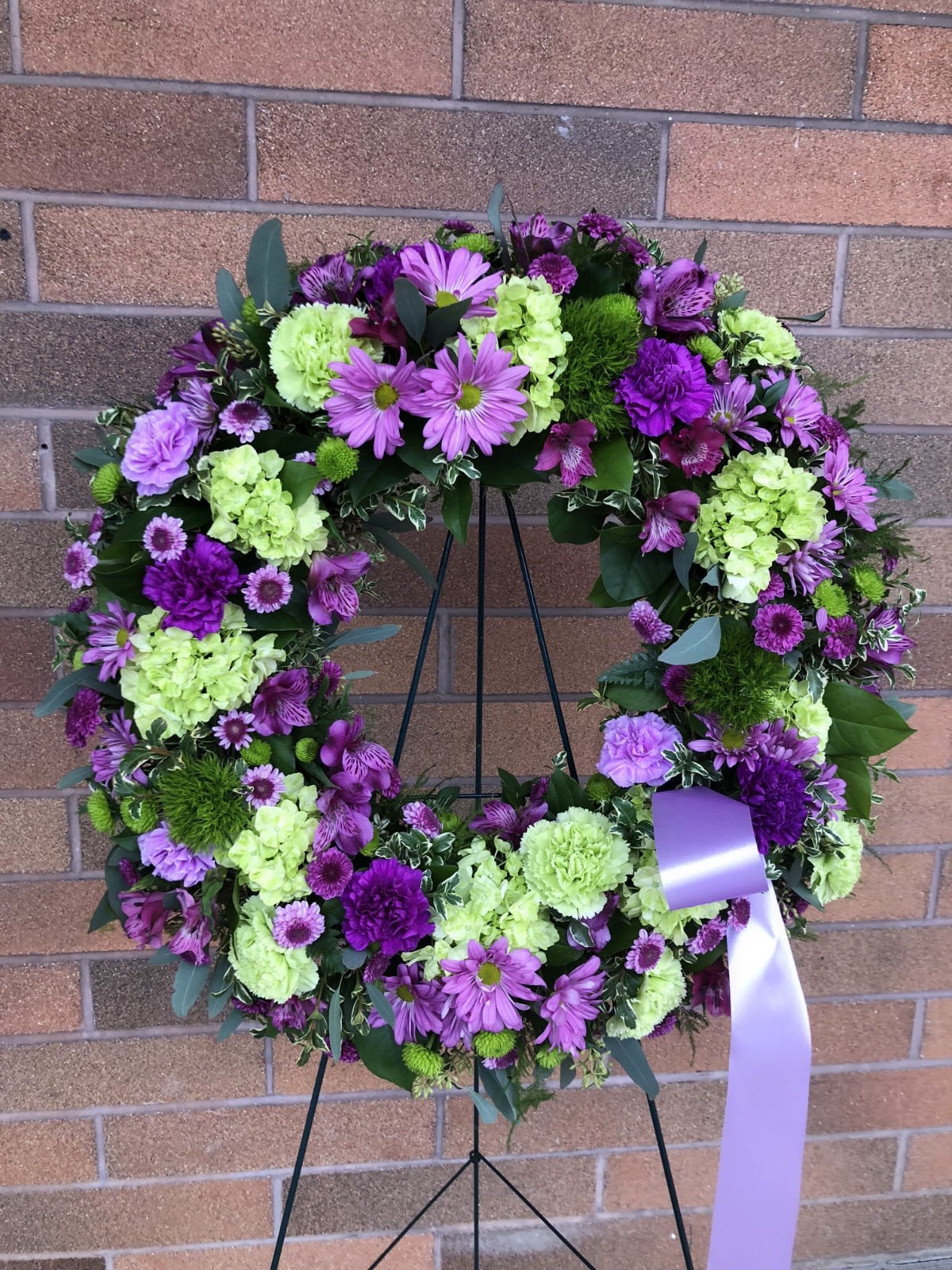 Purple and green floral wreath on a stand with a lavender ribbon