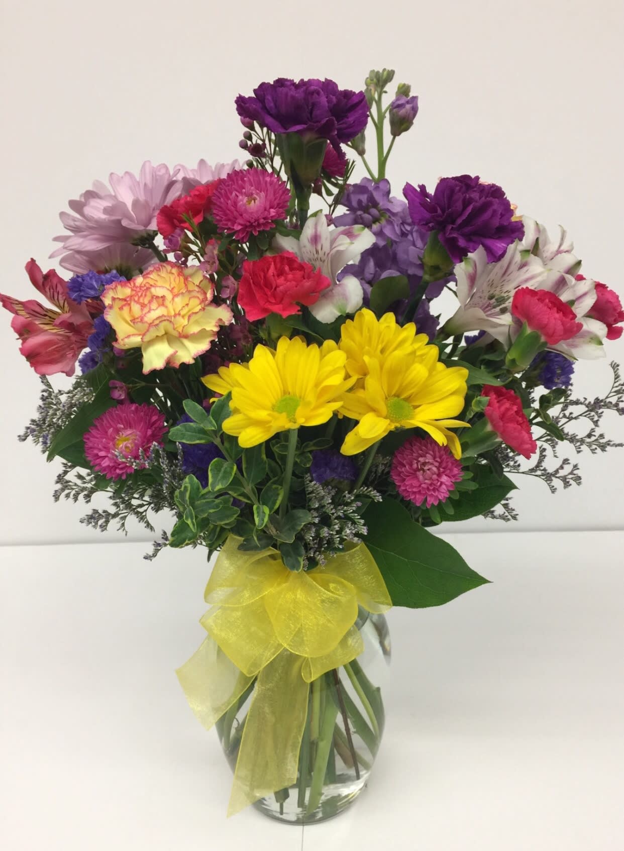 Colorful mixed bouquet in a glass vase with a yellow ribbon