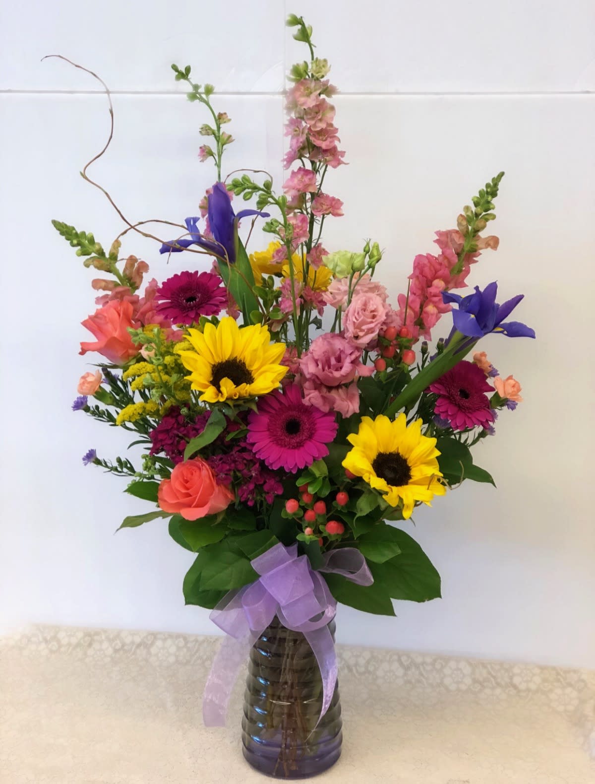 Colorful mixed bouquet in a glass vase with a purple ribbon