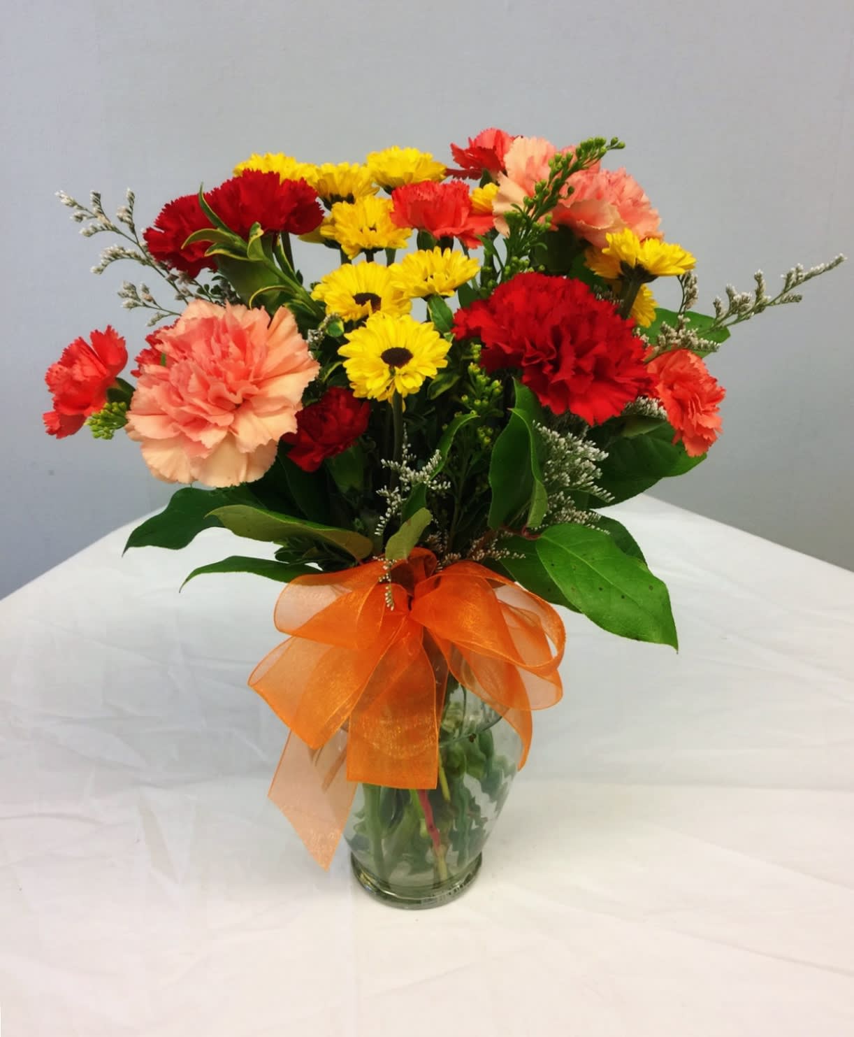 Bouquet of red, yellow, and peach carnations in a glass vase with an orange ribbon