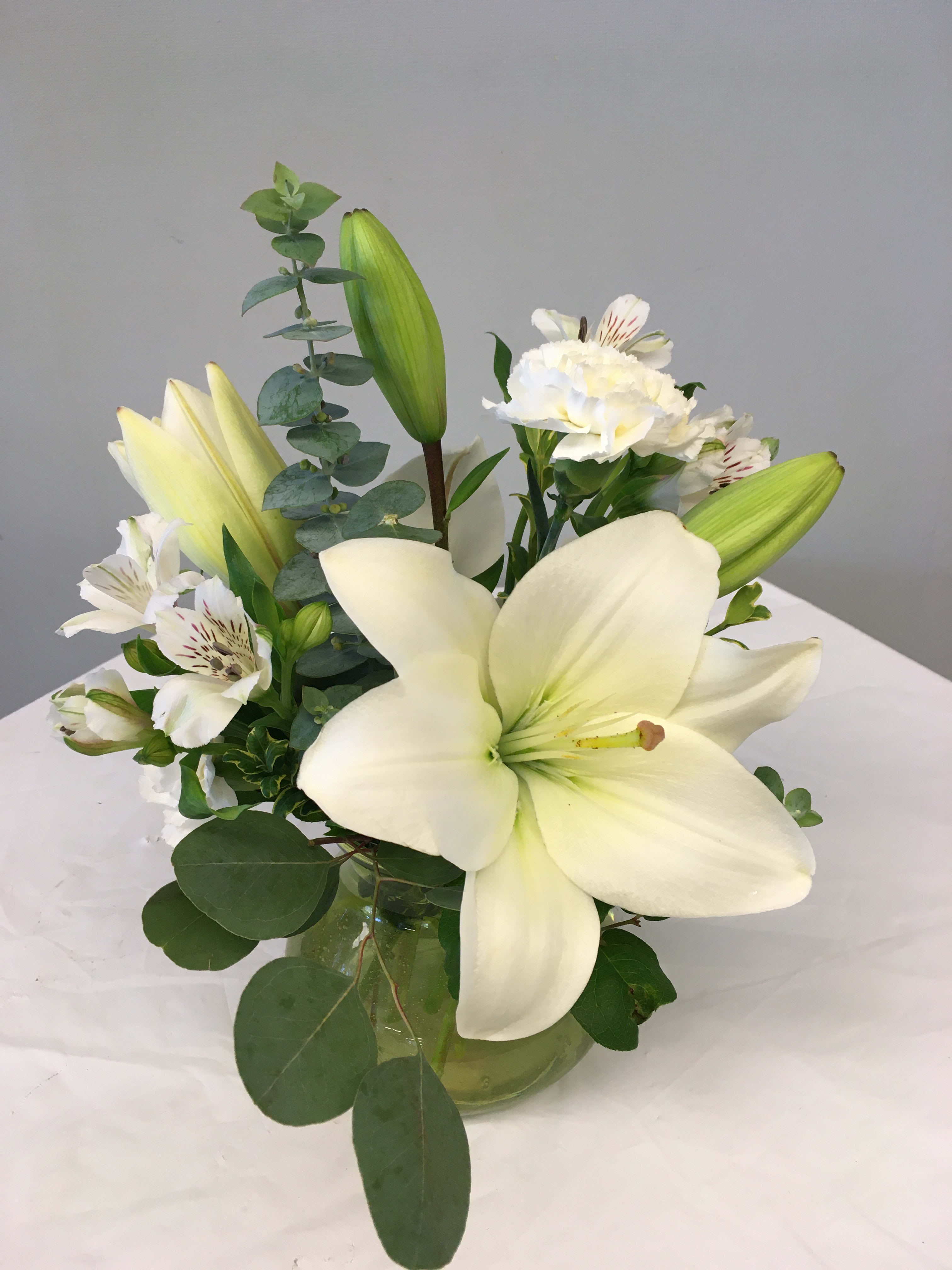 White lilies and alstroemeria arranged in a glass vase.