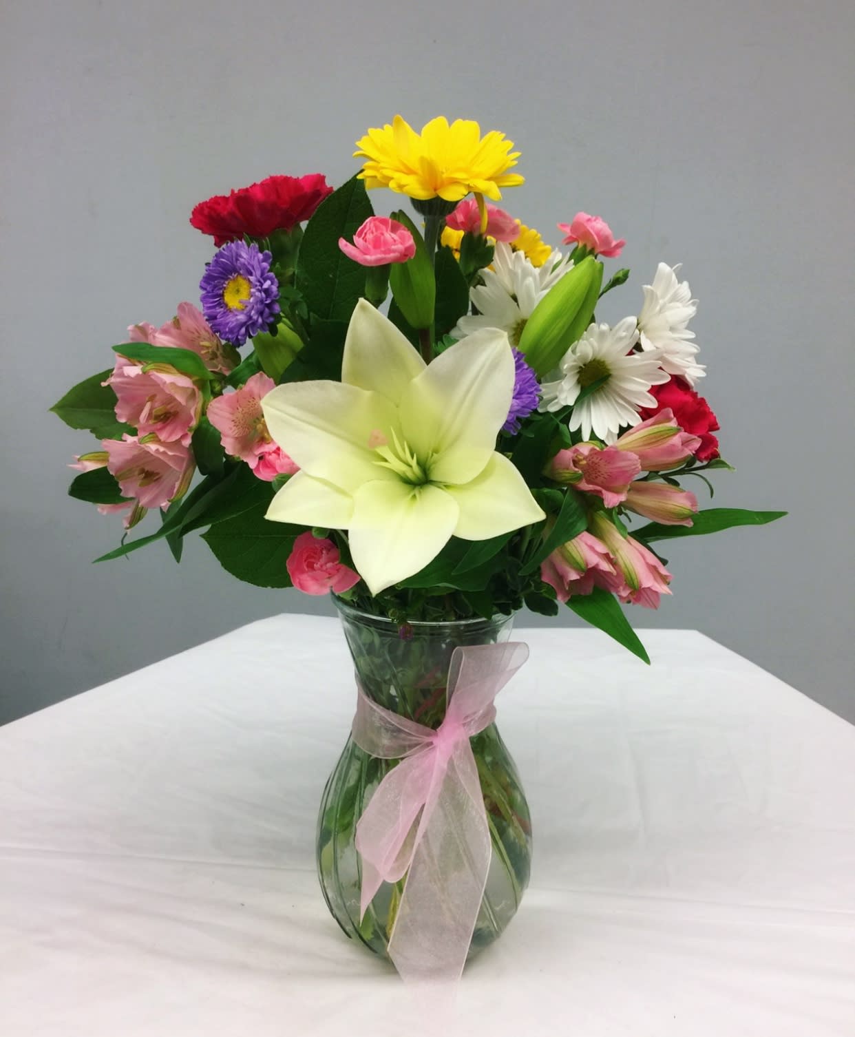 Mixed bouquet with a large white lily in a glass vase tied with pink ribbon