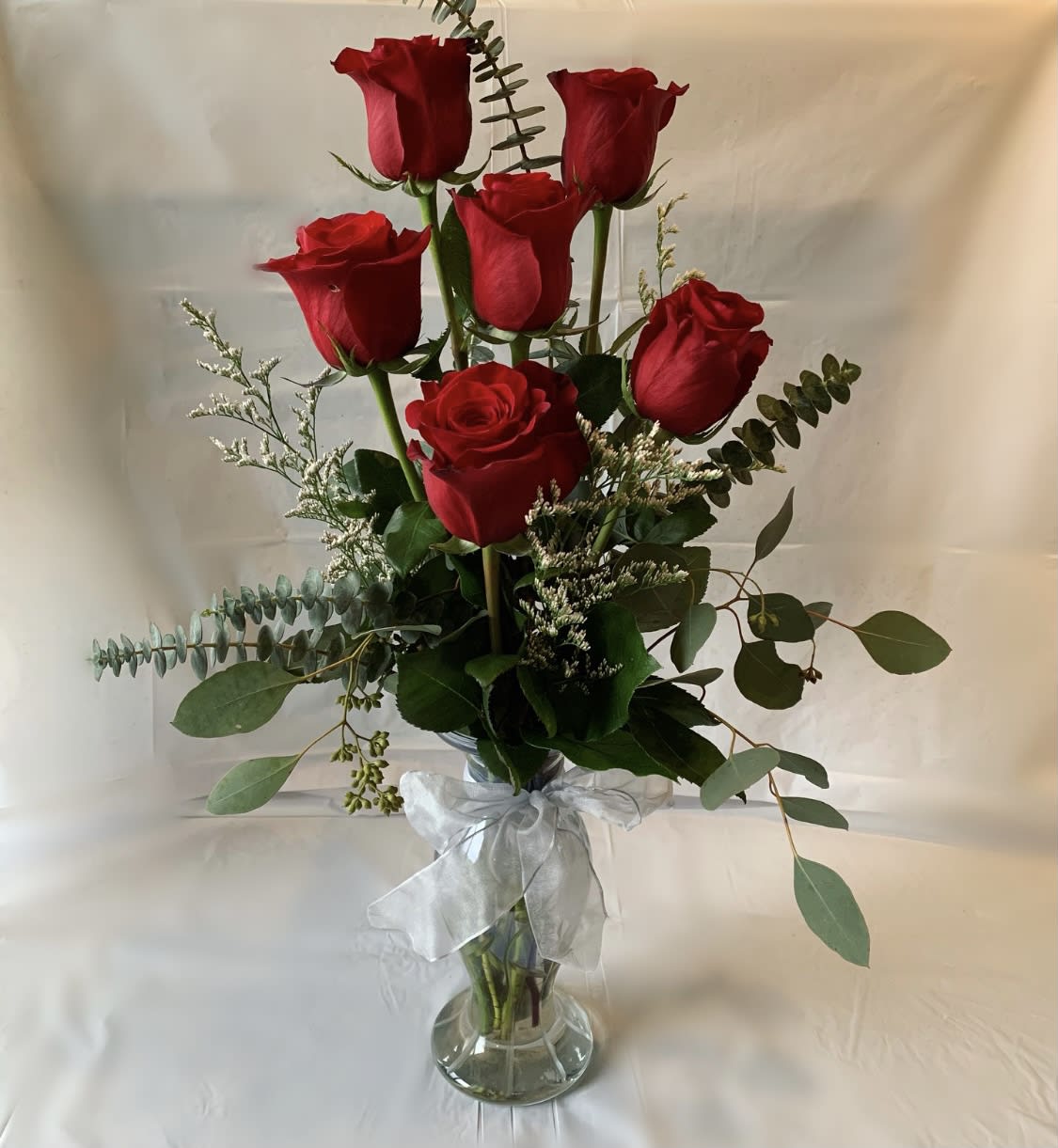 Red roses arranged in a clear glass vase with a white ribbon