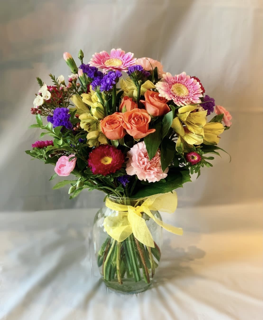 Mixed bouquet of pink, orange, yellow, and purple flowers in a glass vase