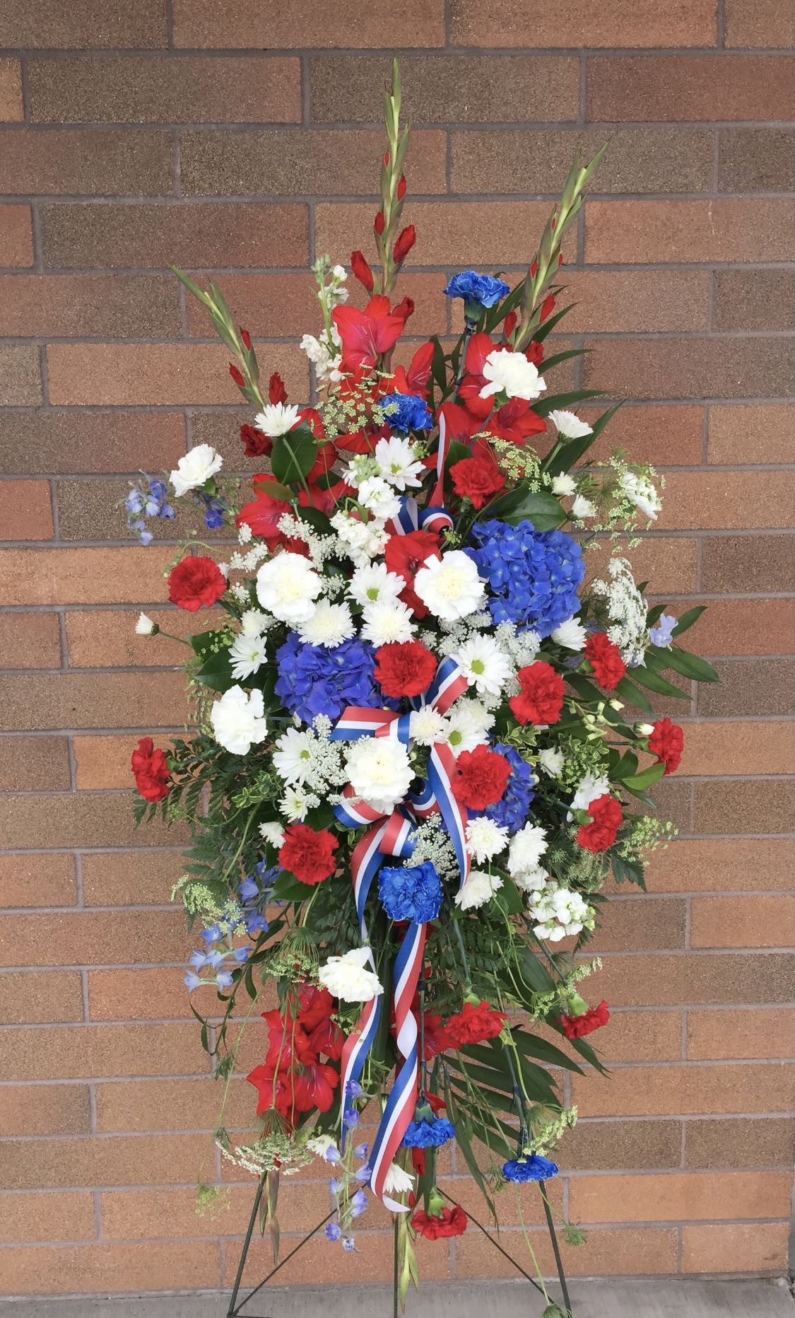 Standing floral wreath with red, white, and blue flowers on a ribboned easel