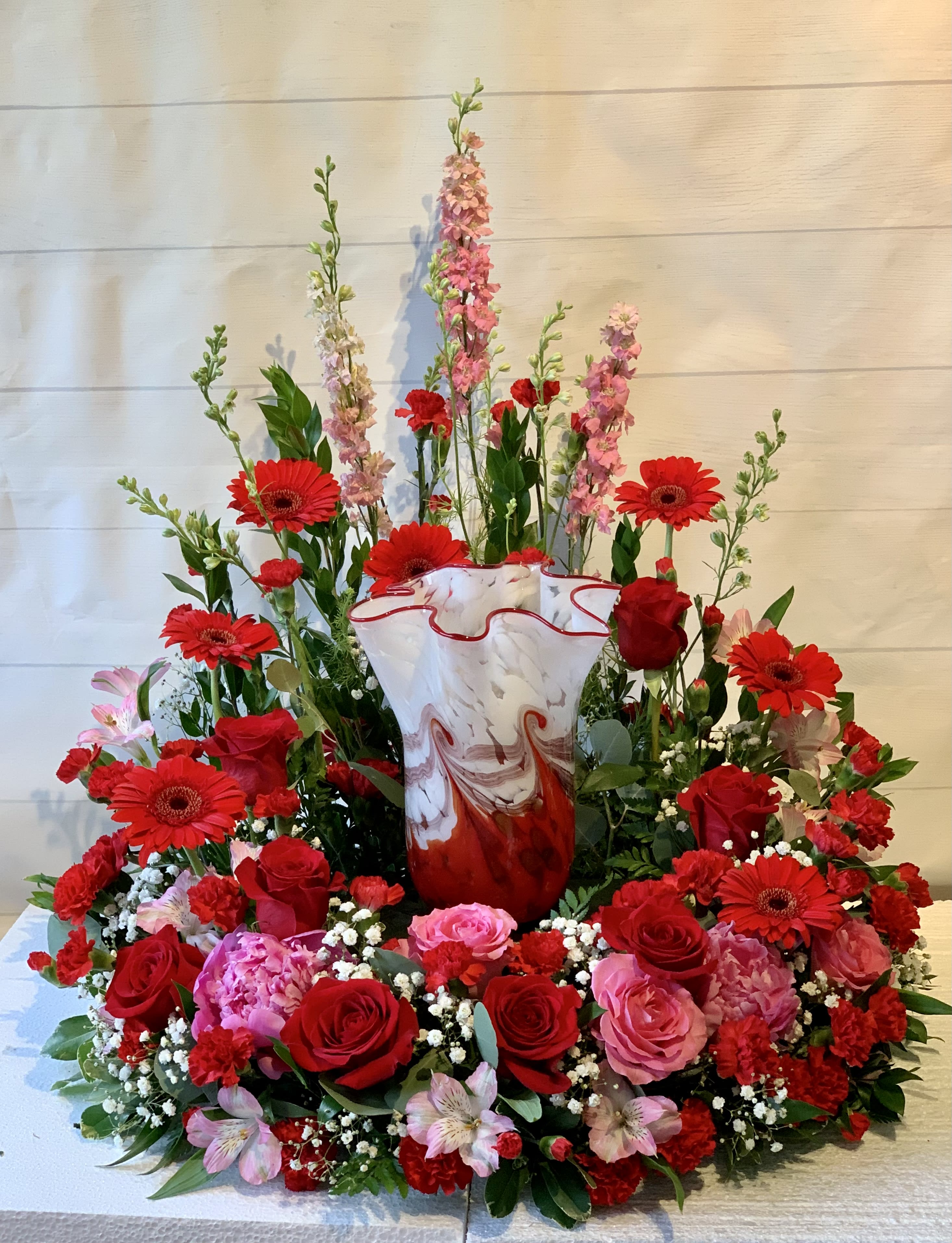 Large red and pink floral arrangement in a marbled vase