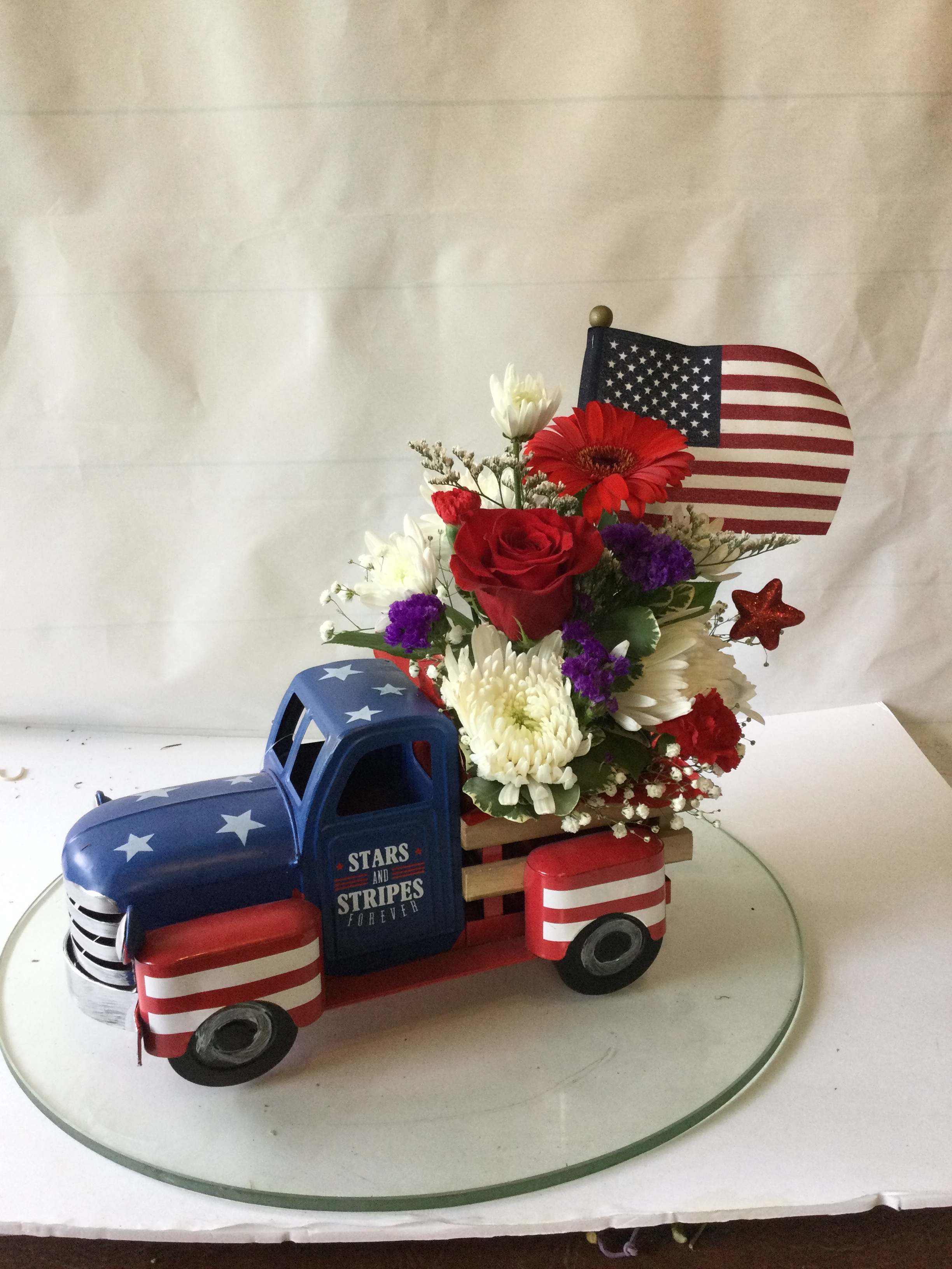 Floral arrangement in a patriotic truck-shaped container with an American flag topper