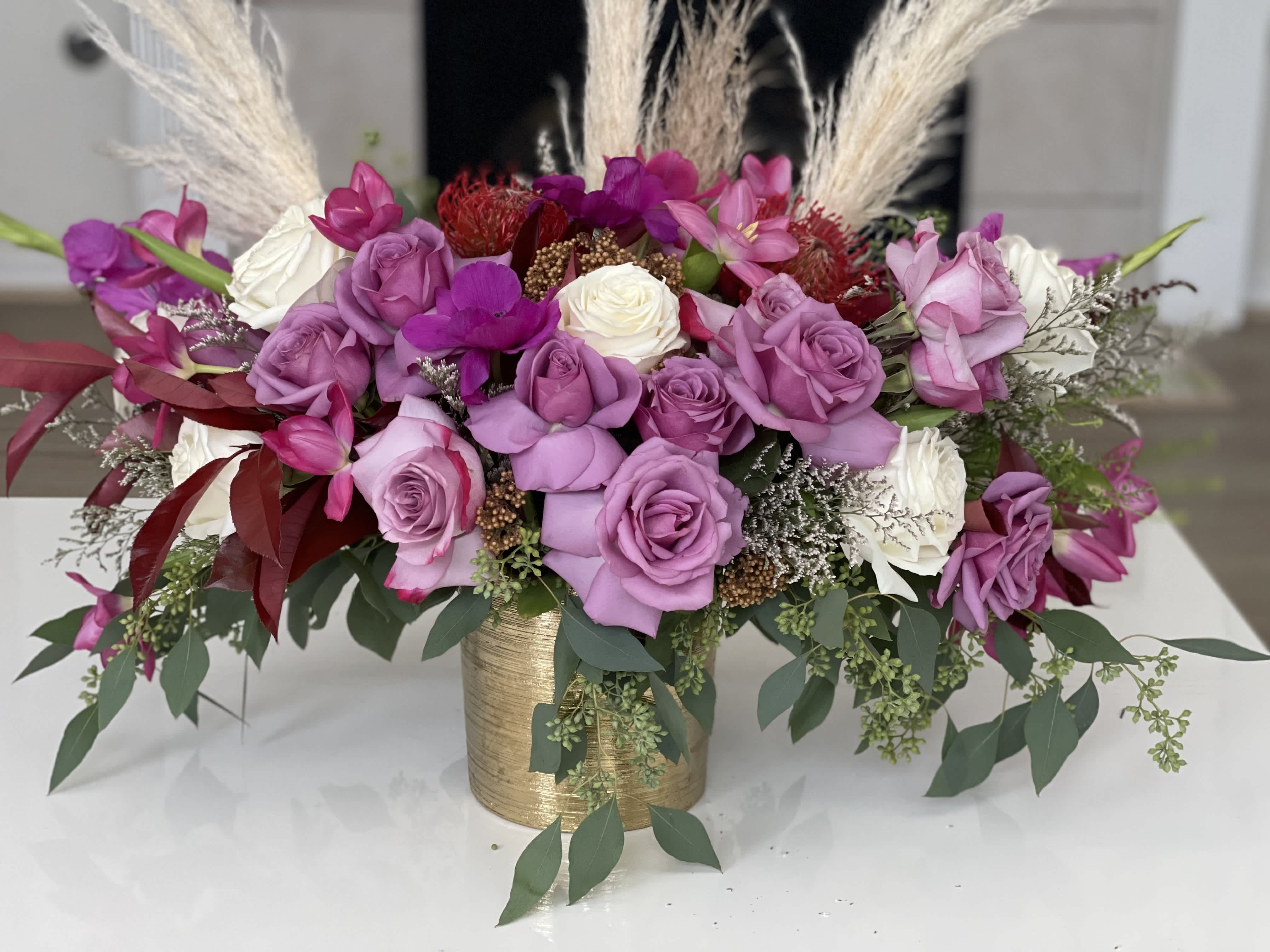 Pink and white roses arranged in a gold vase with tall pampas grass