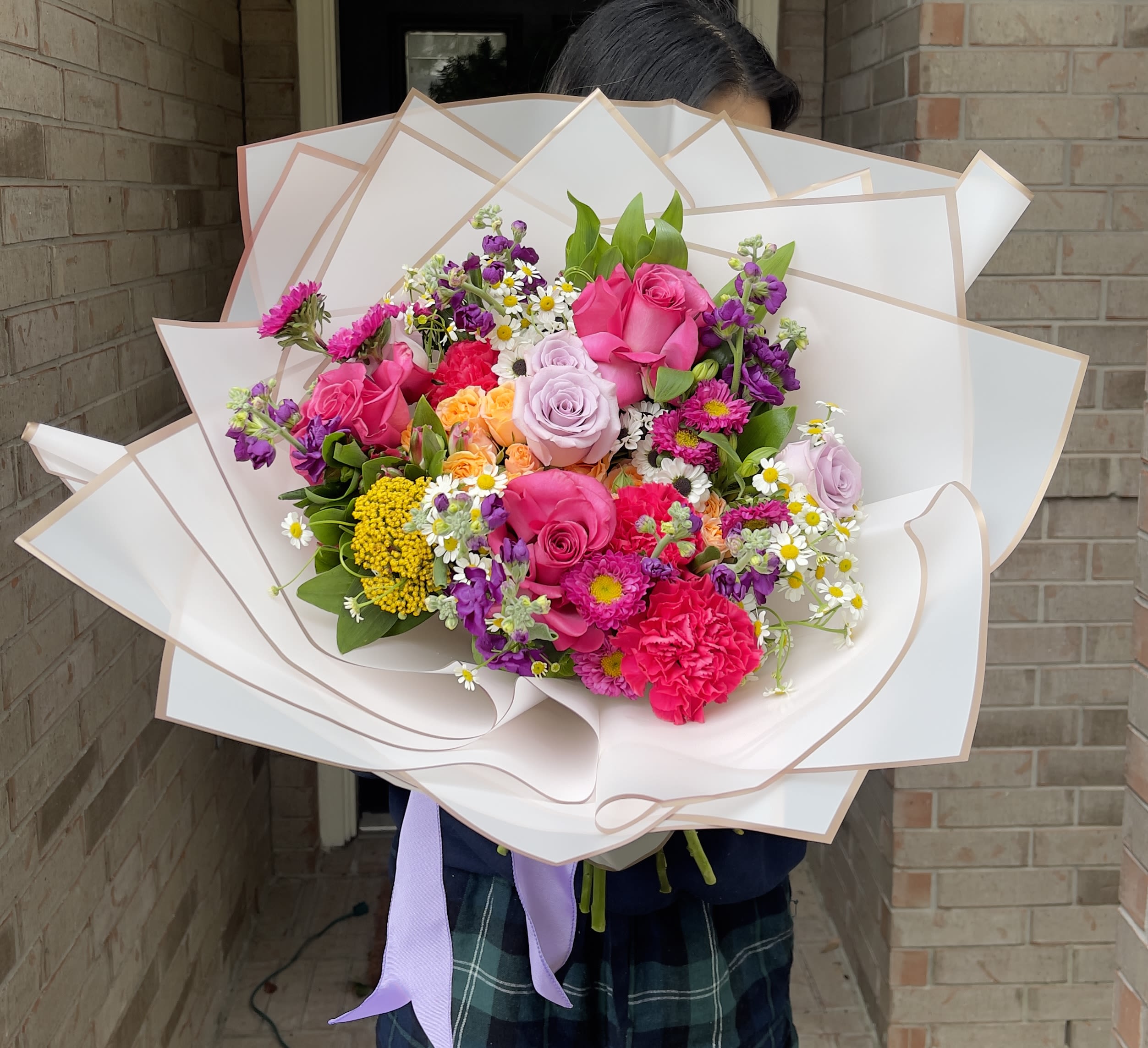 Large bouquet of pink, purple, and yellow flowers wrapped in white paper
