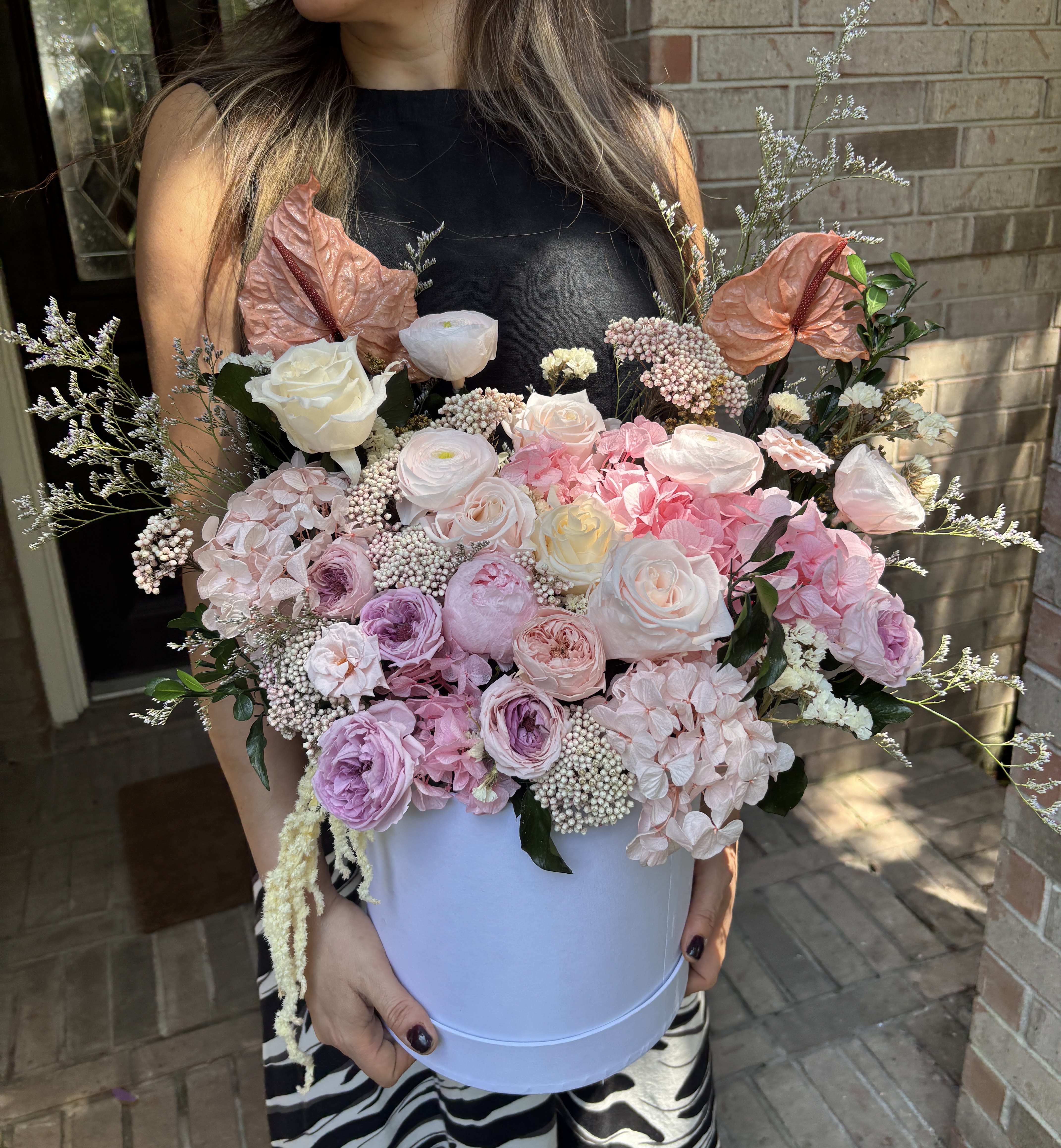 Amaar Long Lasting - Overflowing with real and natural preserved roses, hydrangeas, ranunculus, carnations and airy filler, this long-lasting hatbox arrangement is a romantic birthday bouquet and anniversary gift that feels like a garden captured in pastel. The soft palette of pink, blush, white, lavender and peach-lifted by two prominent peach/copper-toned anthurium accents-creates a gentle, celebratory impression that will make the person you're thinking of feel truly seen and cherished.  Arranged in a white hatbox, the composition is large, full and rounded with layered branching accents that add height and texture while keeping the overall silhouette elegant and modern. Because these are preserved flowers, the arrangement offers the look and tactile presence of fresh blooms with the benefit of lasting beauty for months to come, making it an ideal choice for Mother's Day, weddings, or any special occasion when you want a keepsake gift that continues to delight.