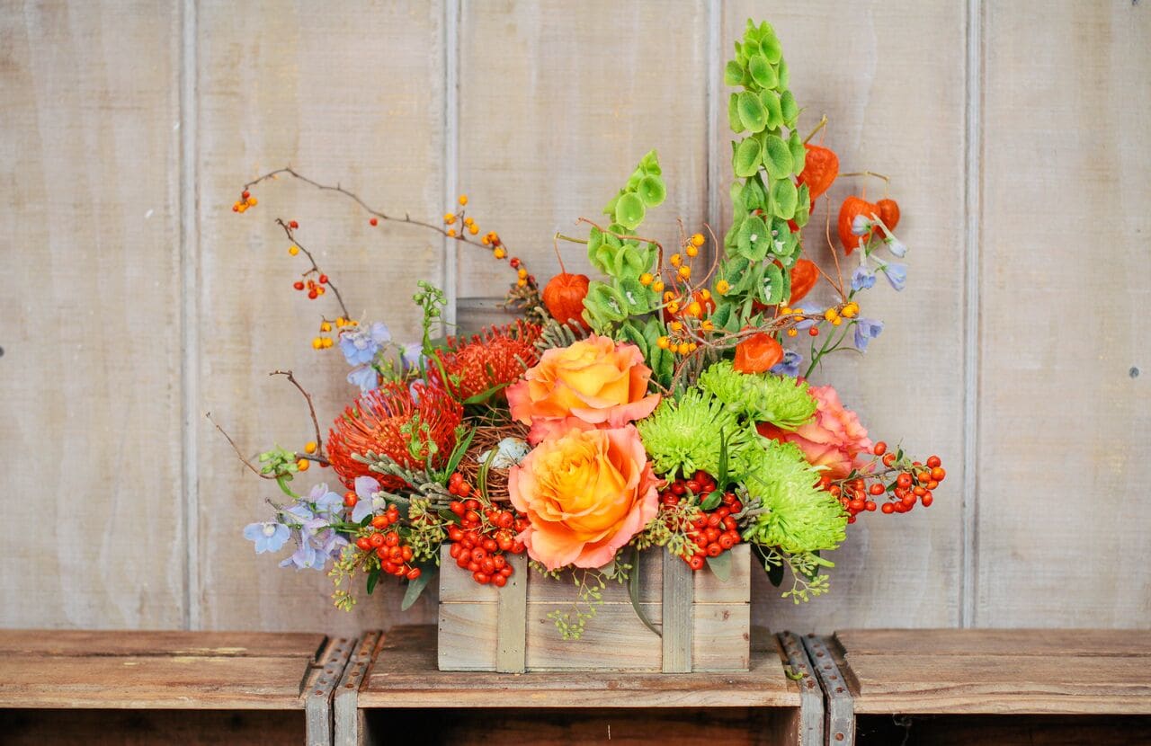 Wooden box arrangement with orange roses, green mums, and berries