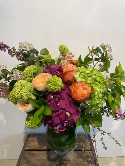 Mixed bouquet of orange roses, green hydrangeas, and purple blooms in a glass vase