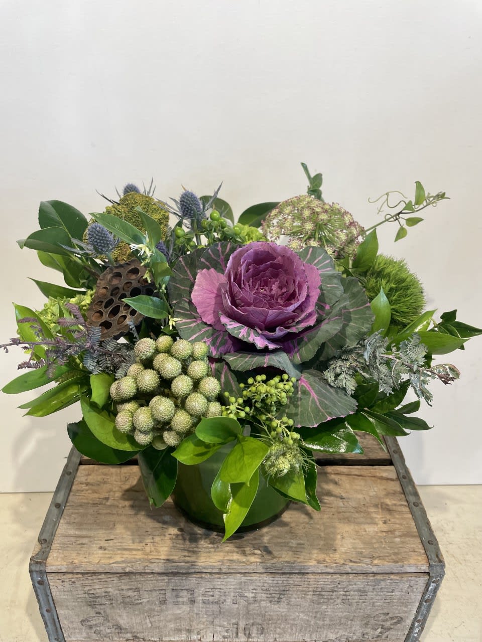 Purple ornamental cabbage arrangement in a green container with mixed foliage