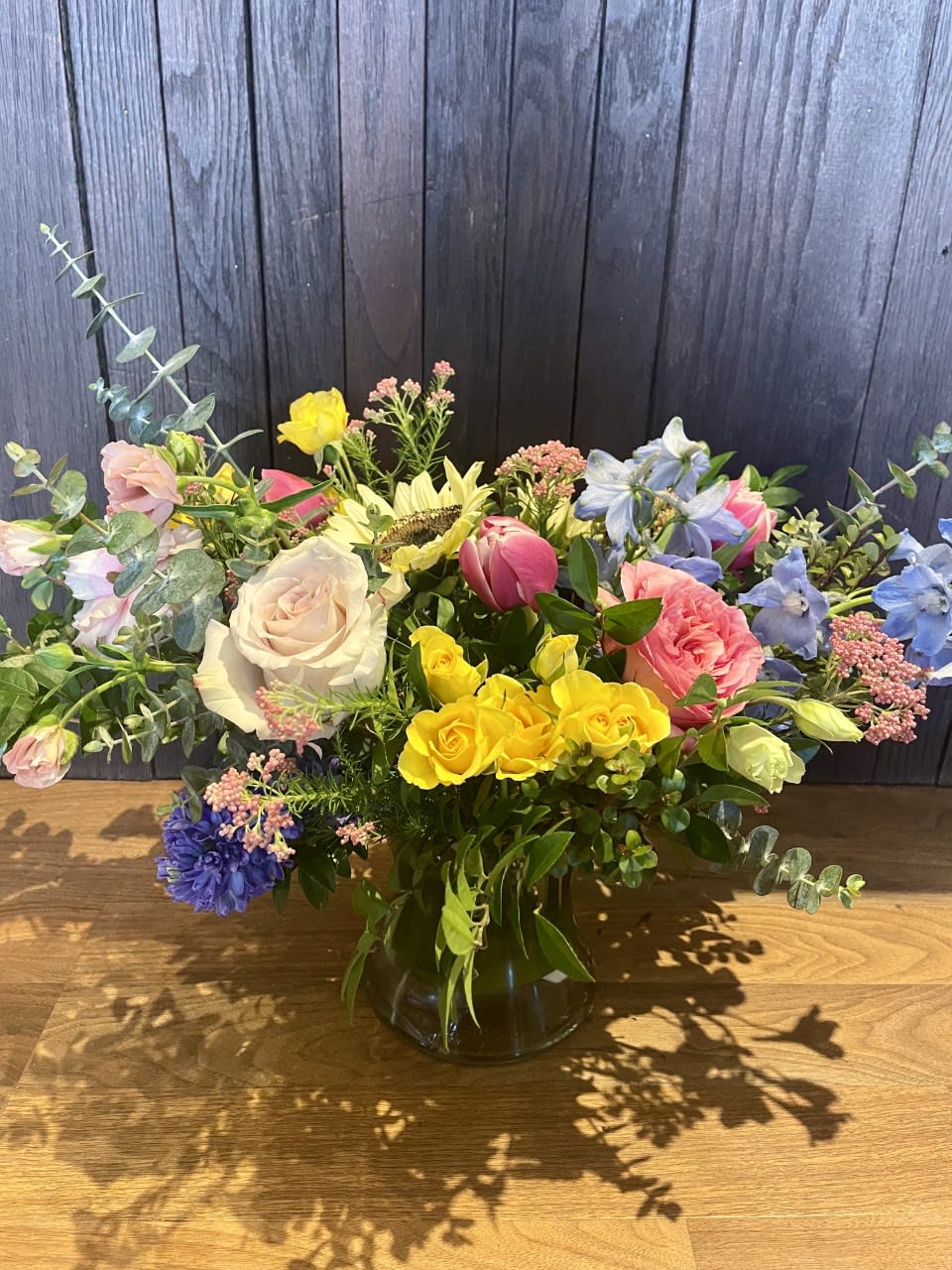 Mixed bouquet in a glass vase with roses, tulips, and blue flowers