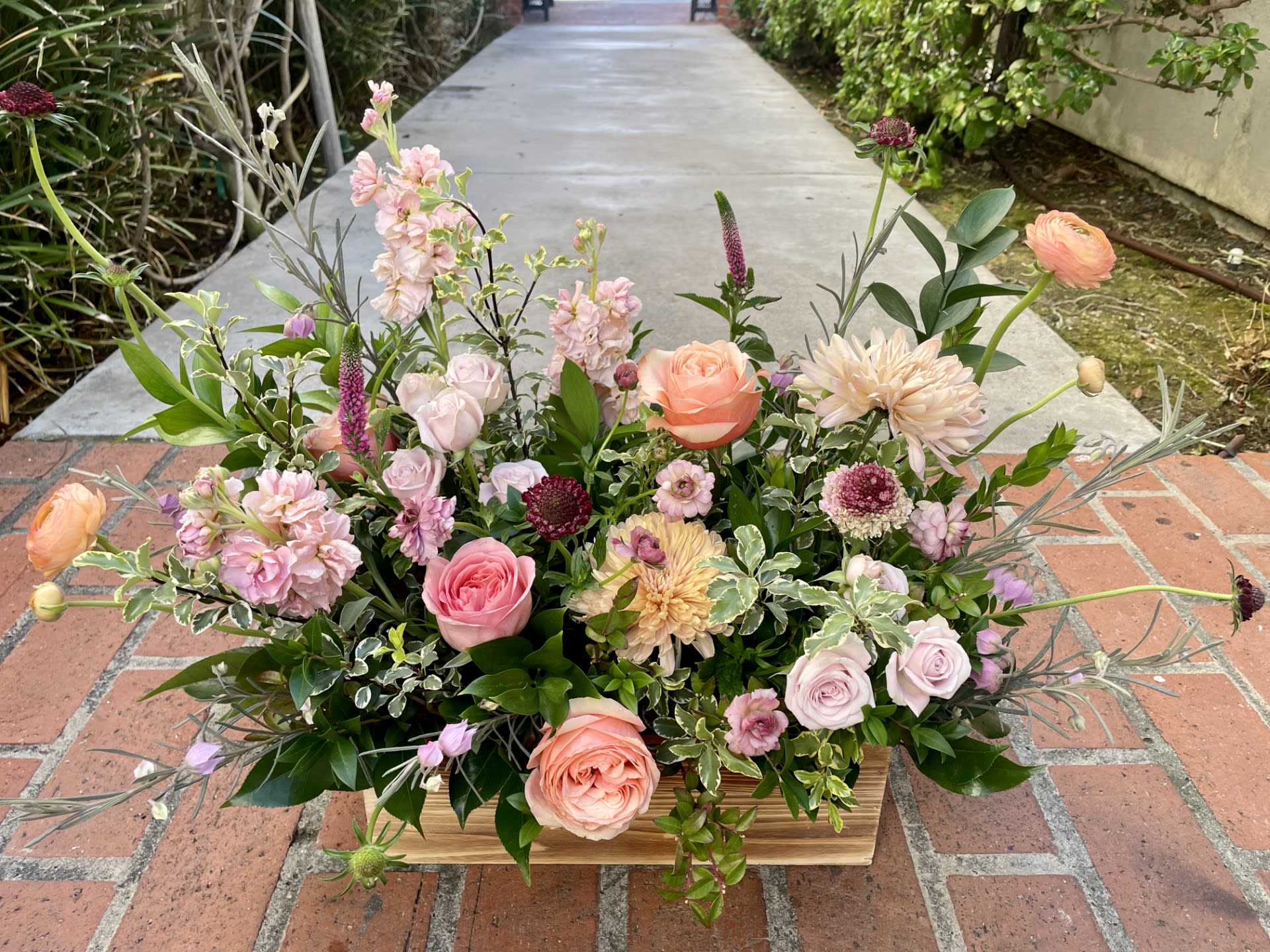 Low floral arrangement with pink, peach, and lavender blooms in a wooden container