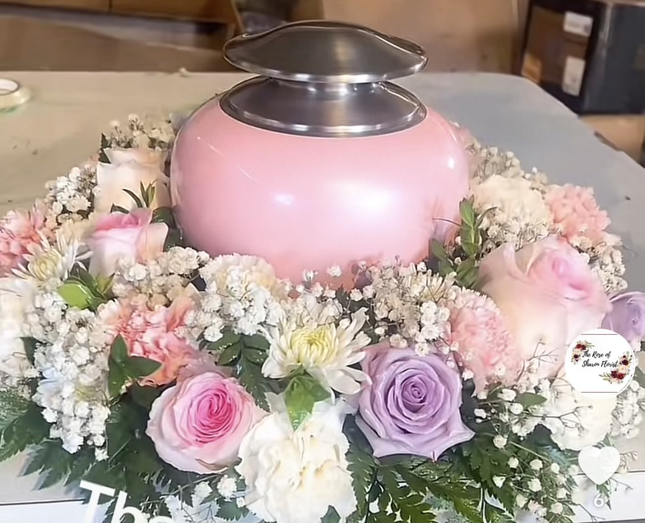 Pink urn surrounded by pastel roses and white filler flowers