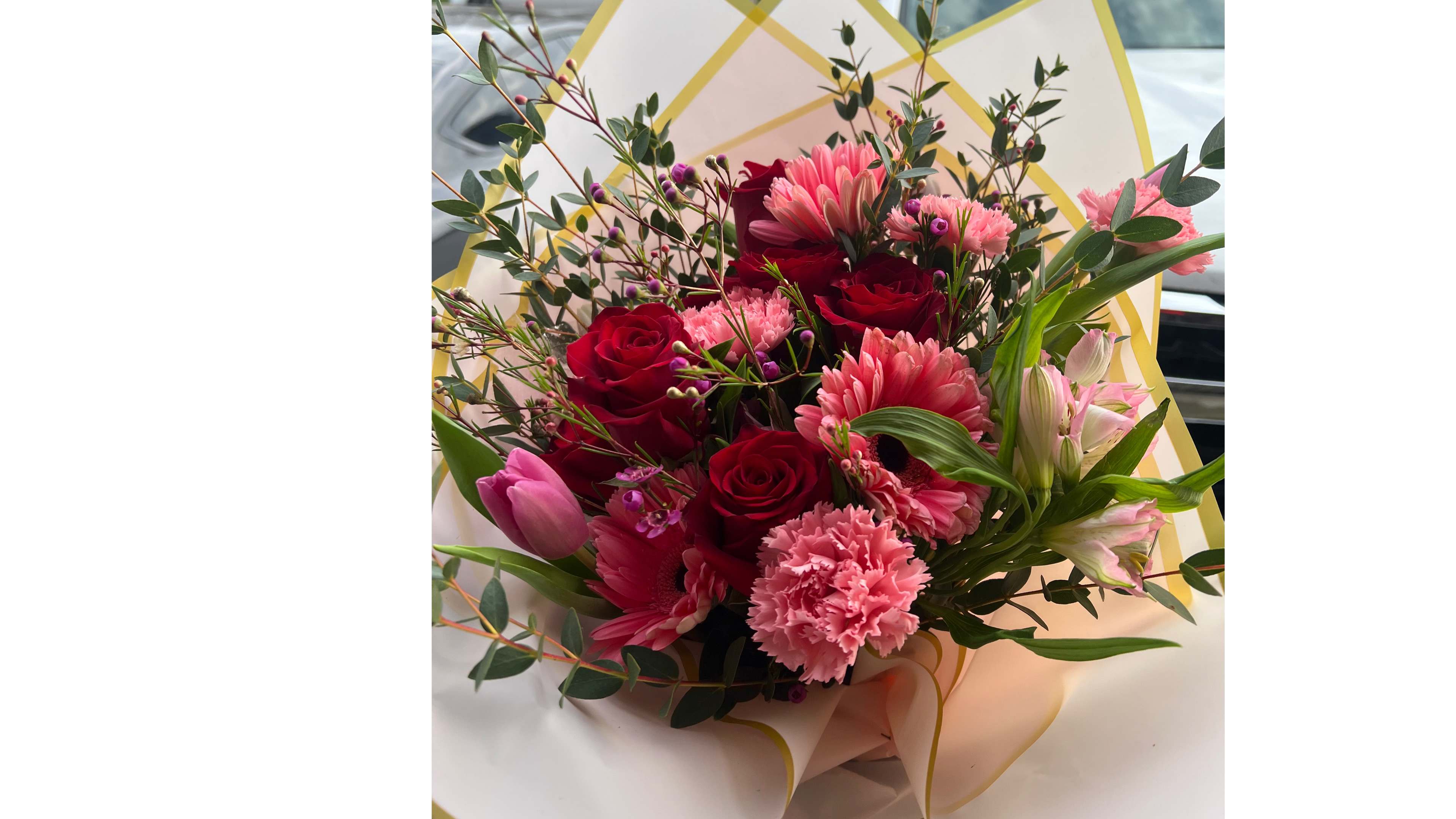 Hand-tied bouquet of red roses and mixed pink flowers wrapped in pale paper