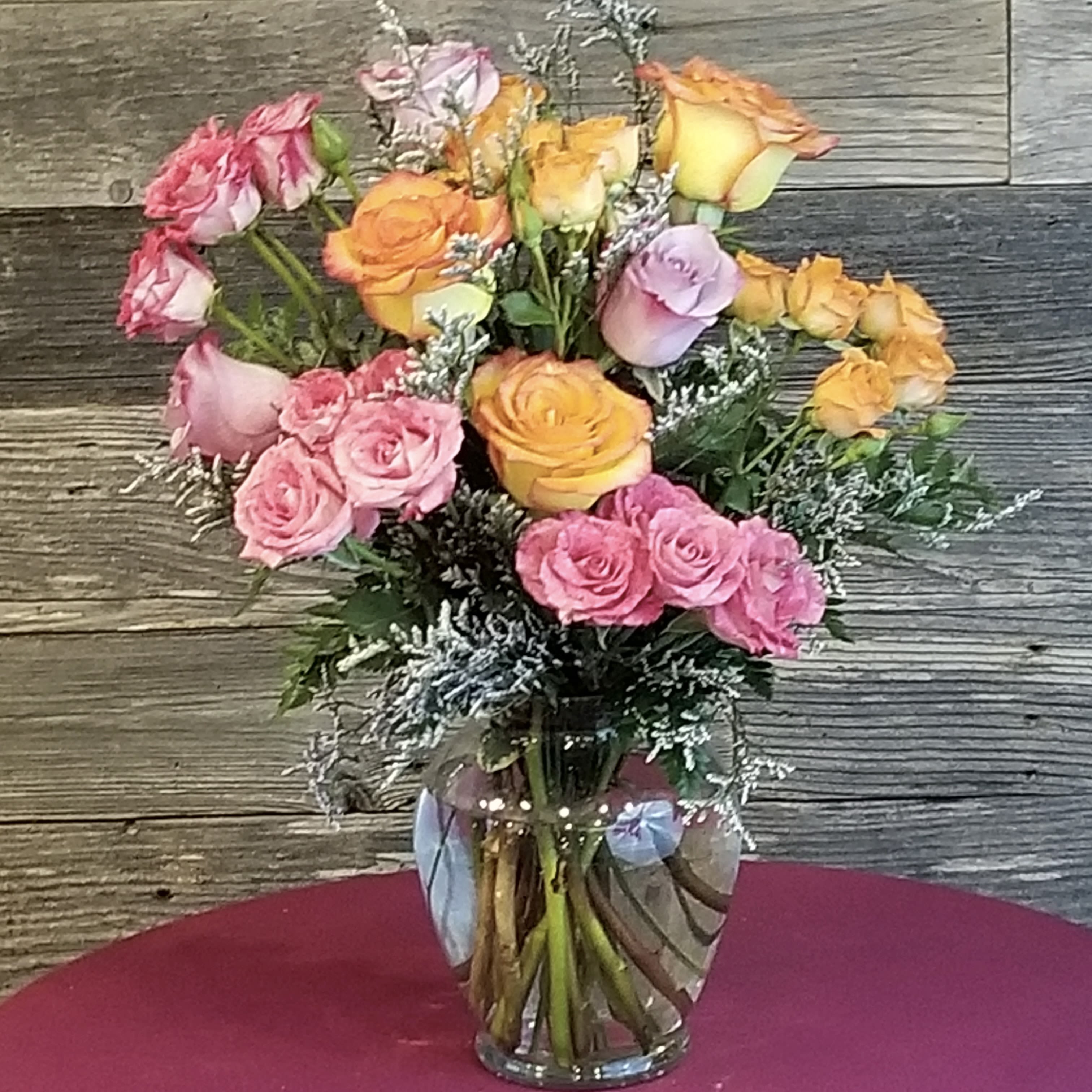 Arrangement of pink, orange, and yellow roses with white filler flowers in a clear glass vase.