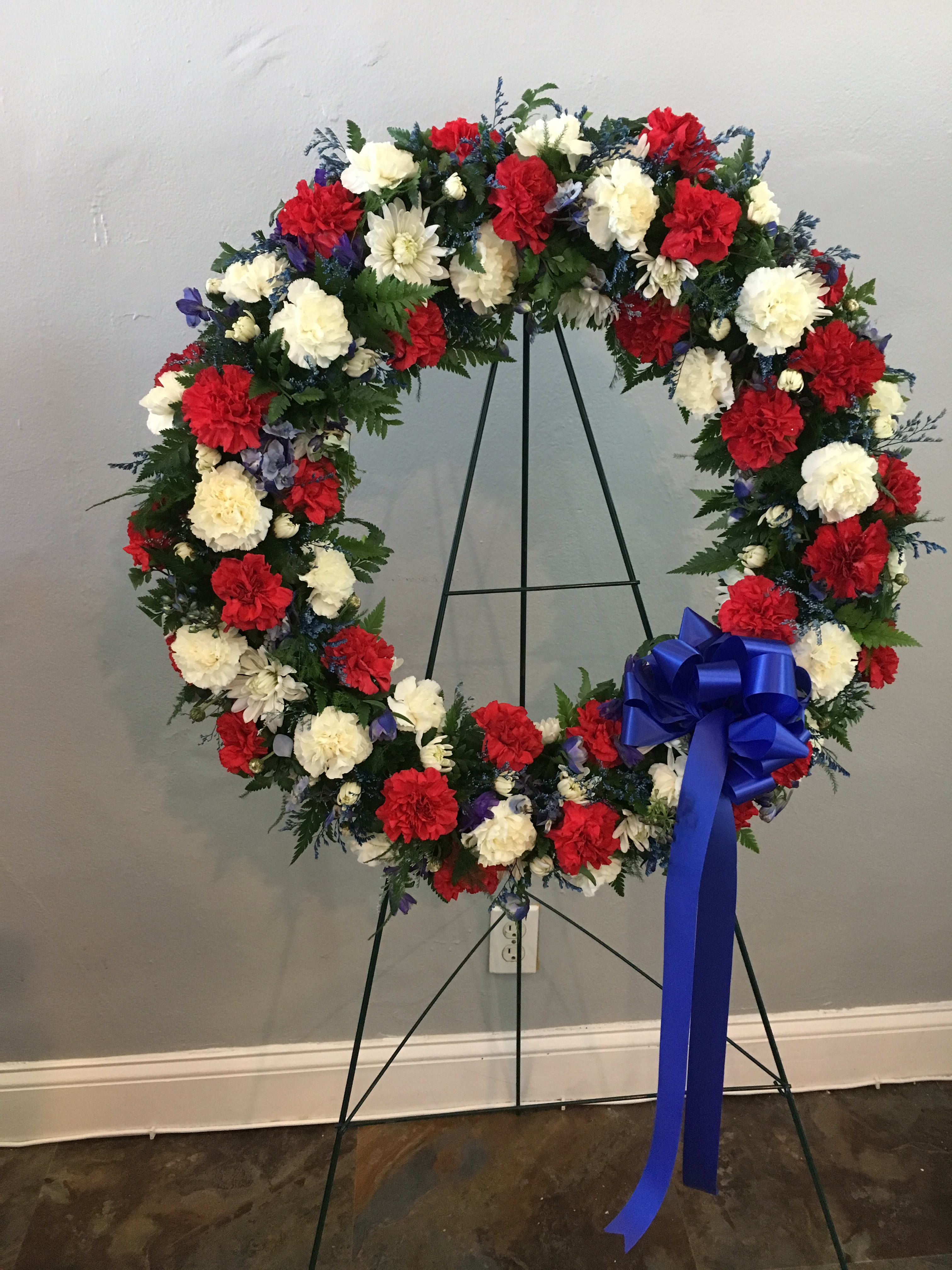 Circular wreath of red, white, and blue flowers on a stand with a blue bow