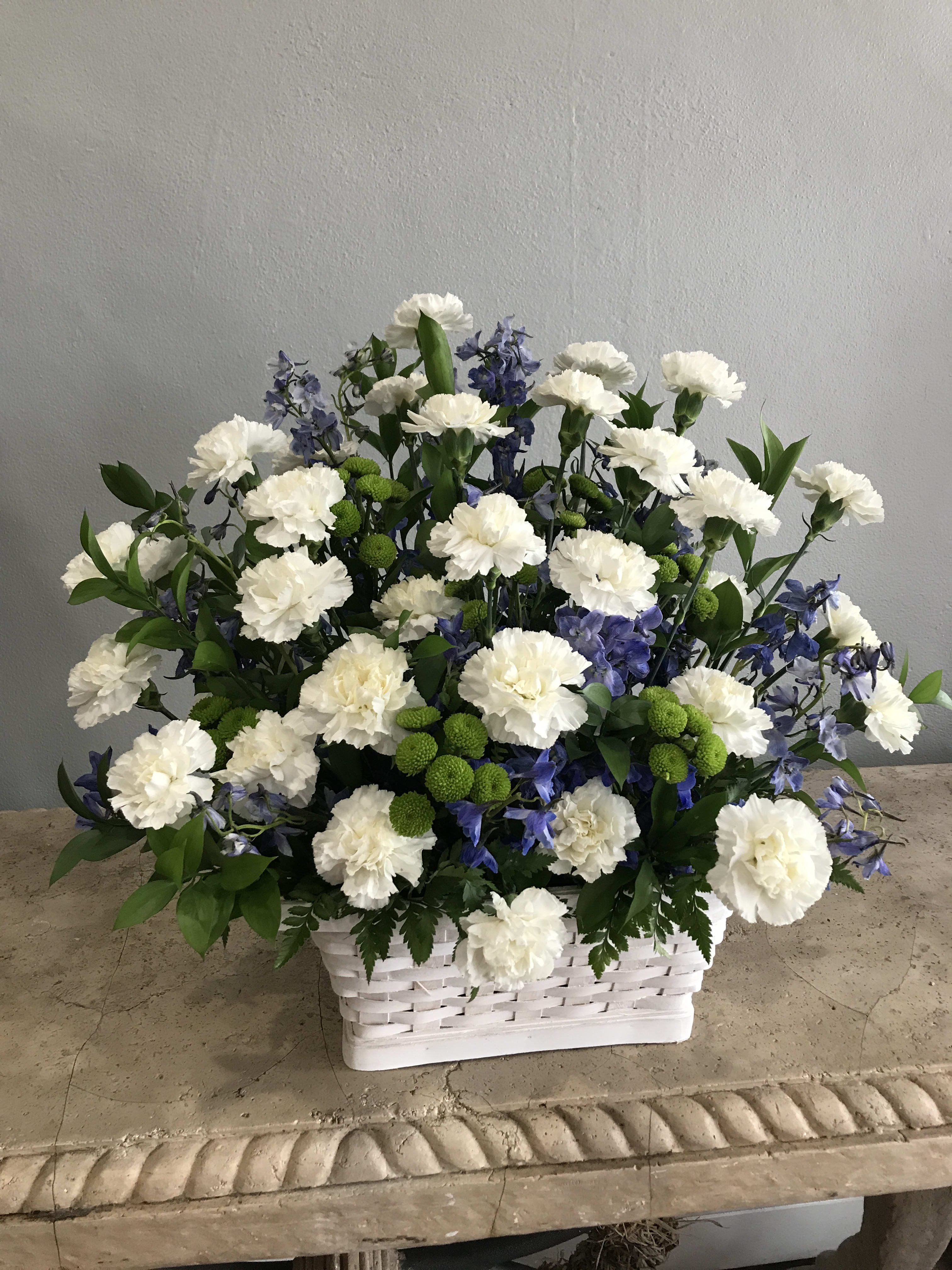 White carnations and blue flowers arranged in a white basket
