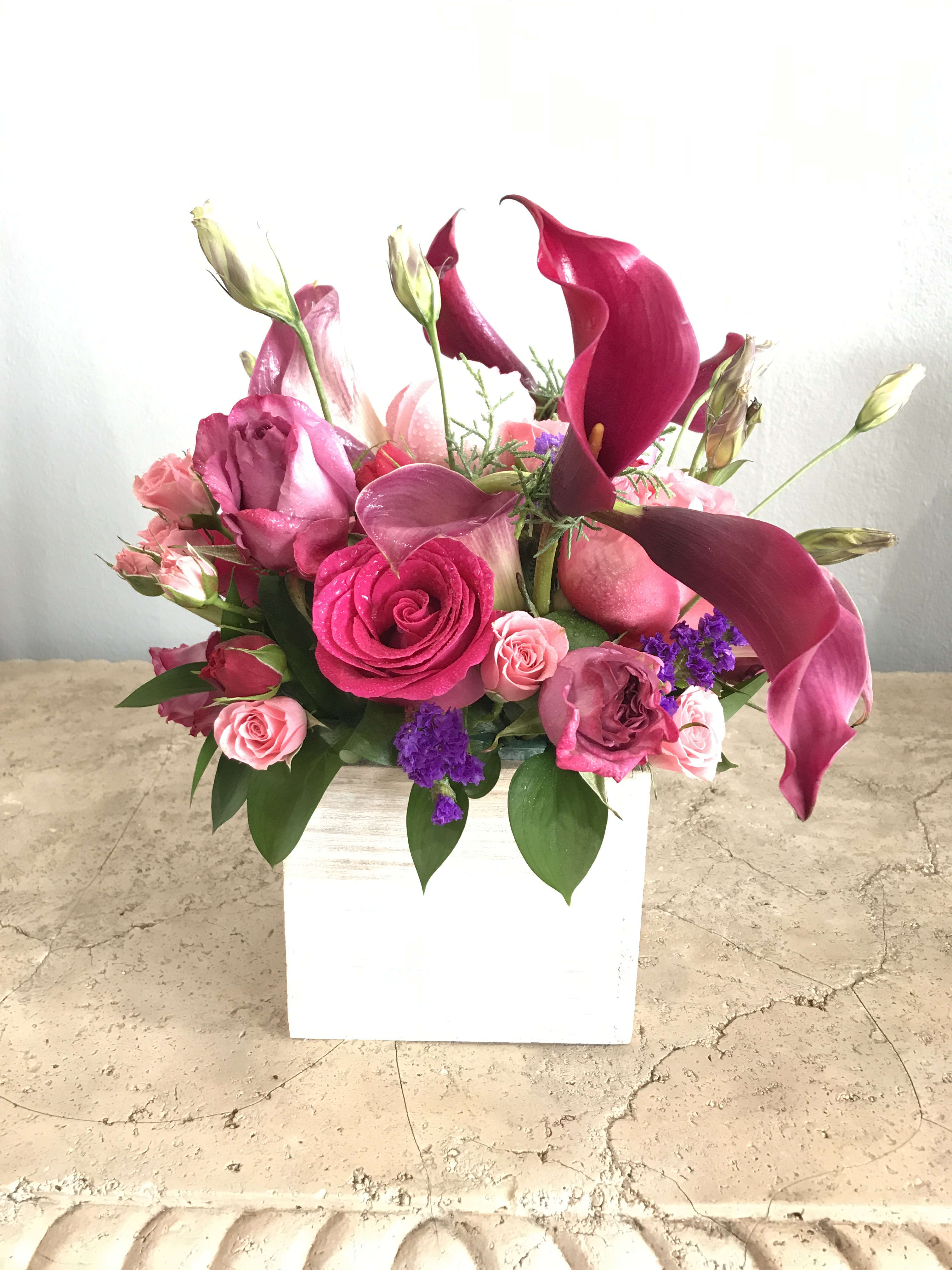 Pink and magenta floral arrangement in a white square vase