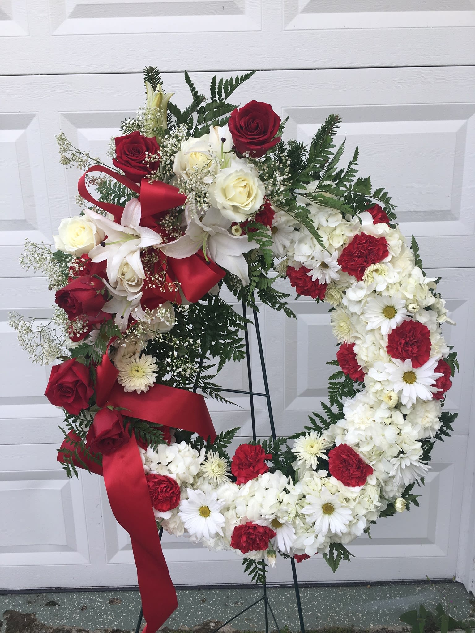 Red and white floral wreath on a stand with ribbon