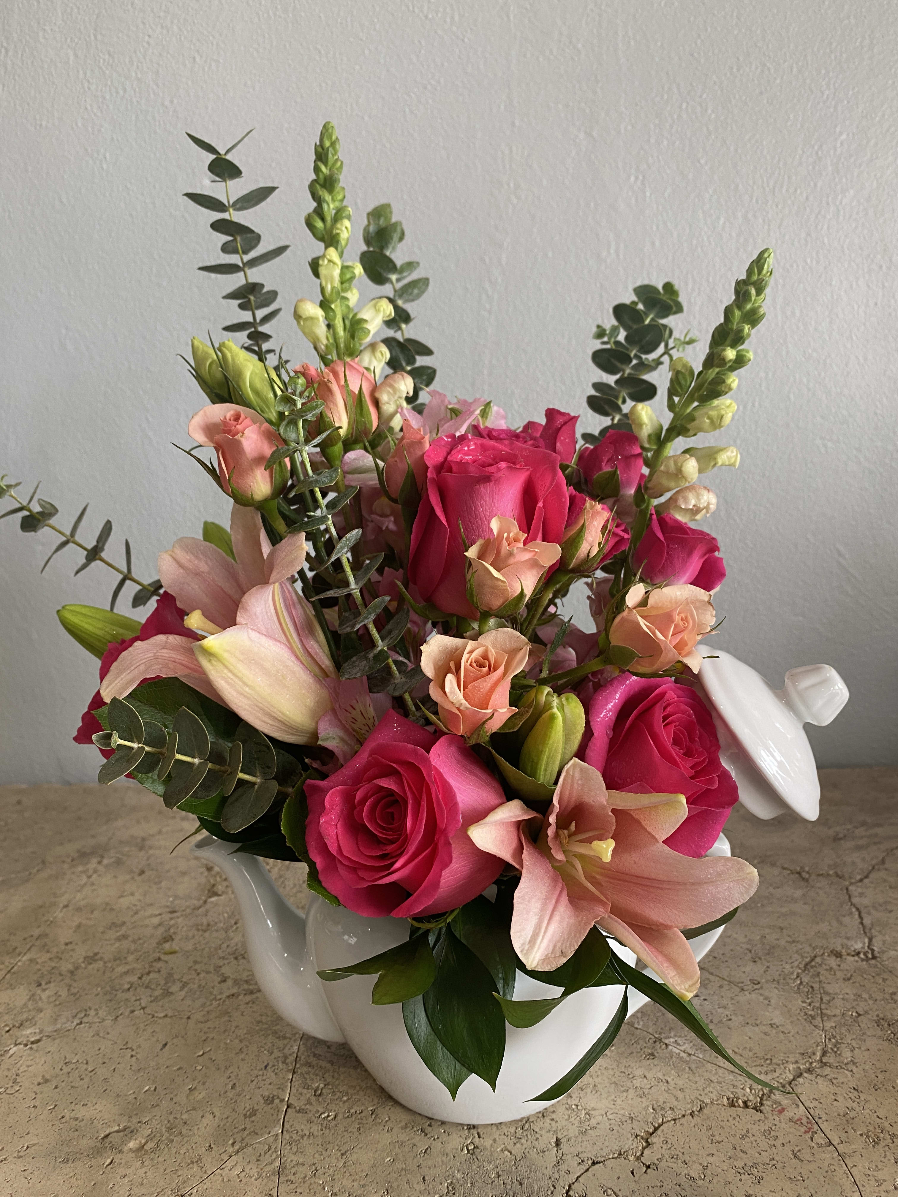 Pink roses and lilies arranged in a white ceramic teapot.