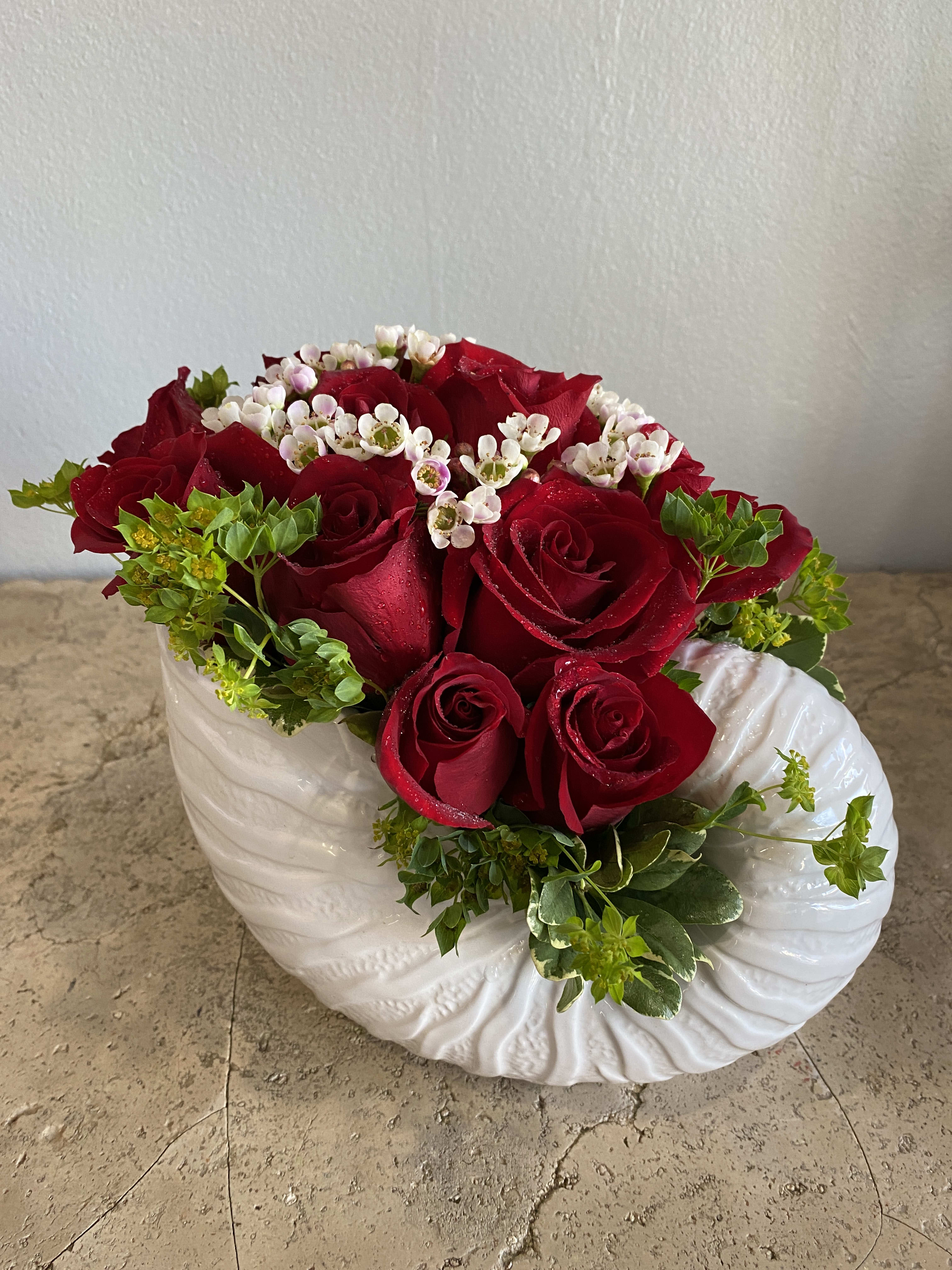 Red roses and white filler flowers in a white ceramic vase