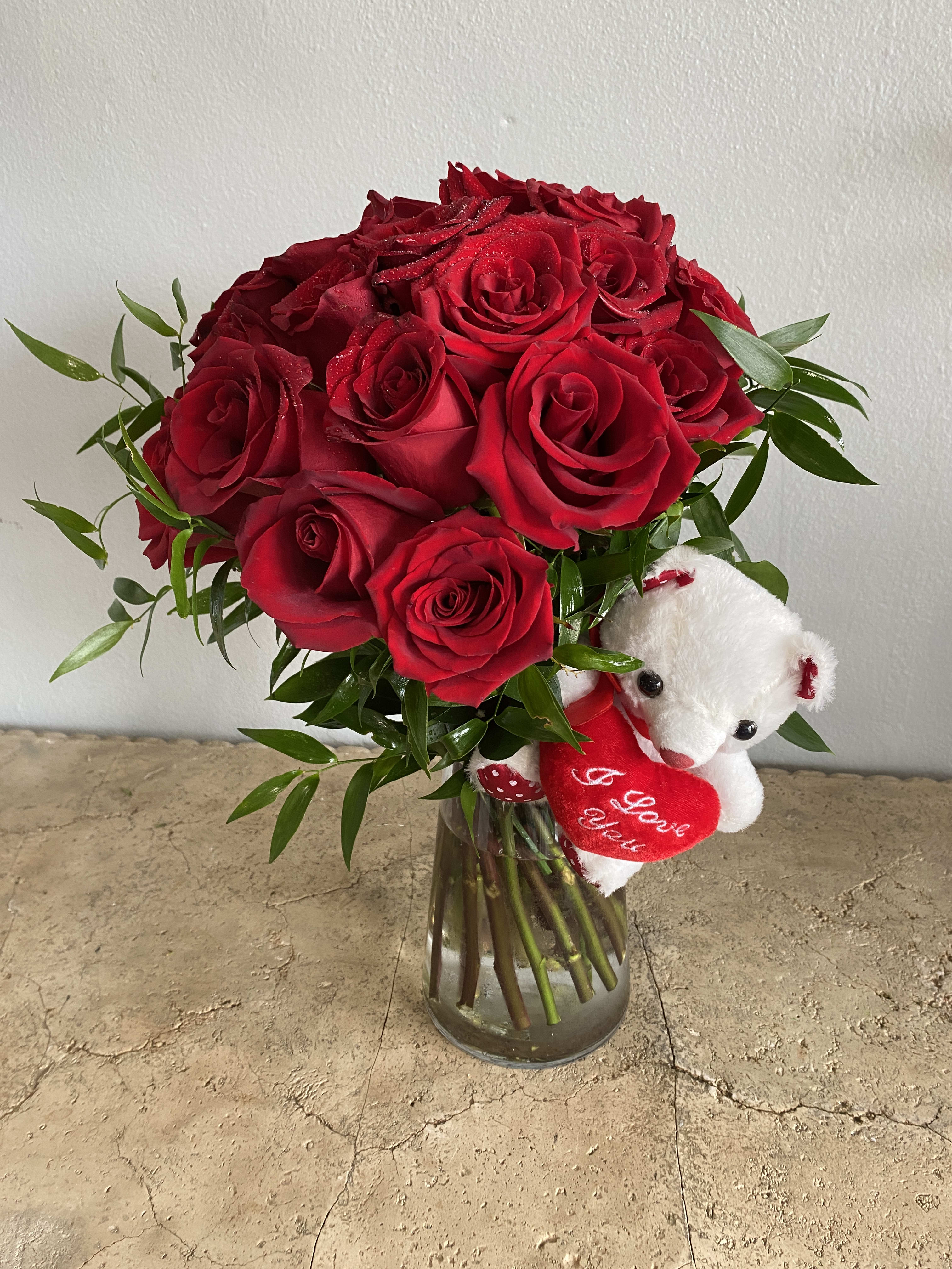 Red roses in a glass vase with a small white teddy bear