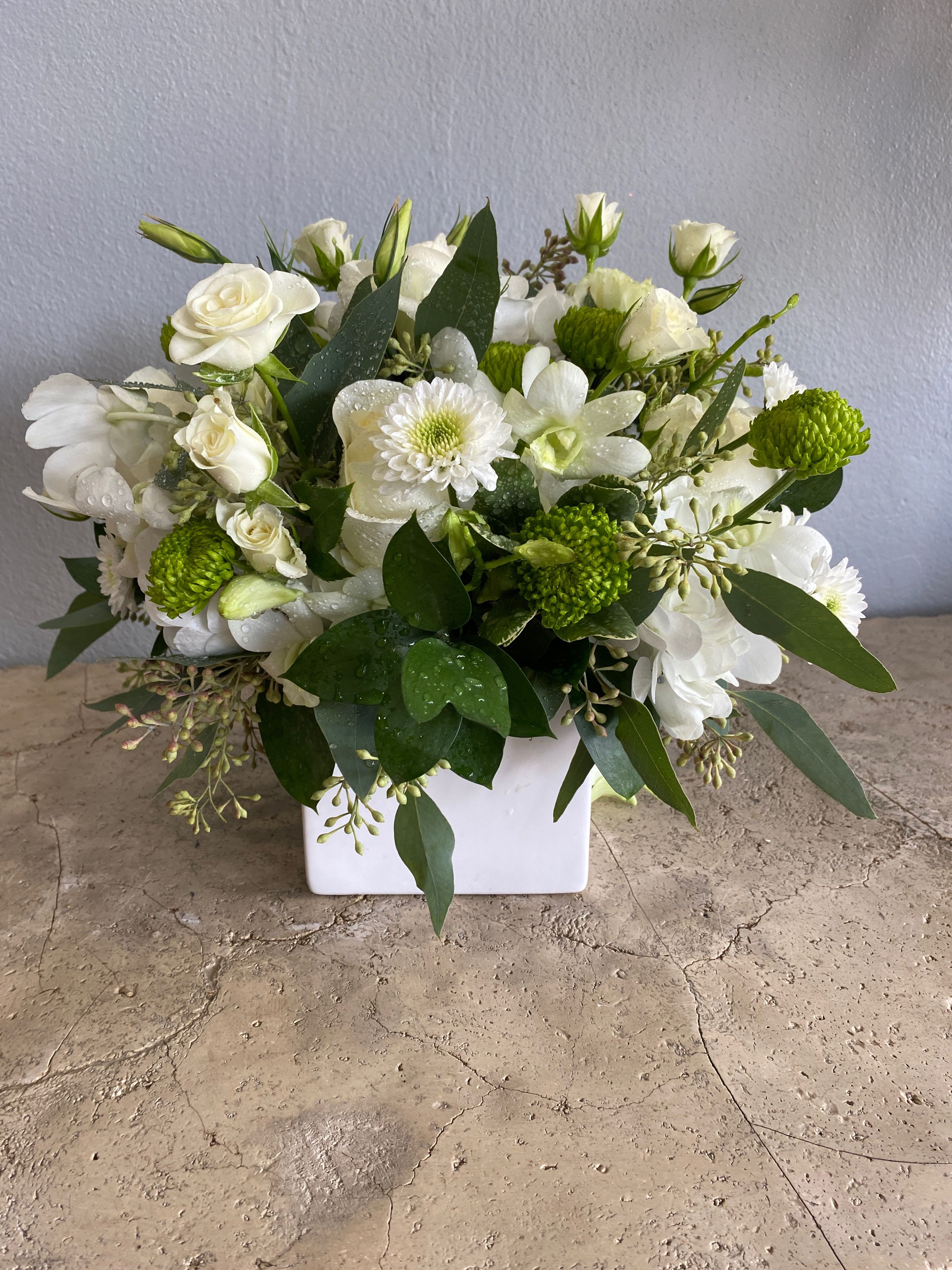 White floral arrangement in a square vase with green accents