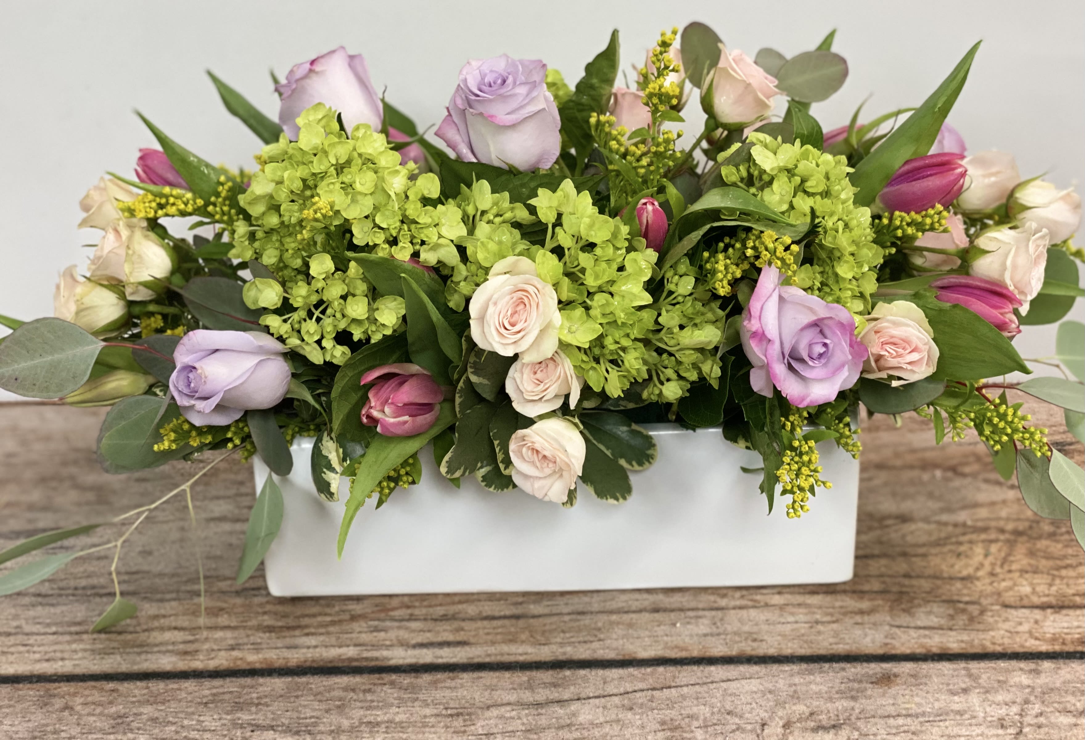 Rectangular floral arrangement with pastel roses and green hydrangeas in a white vase