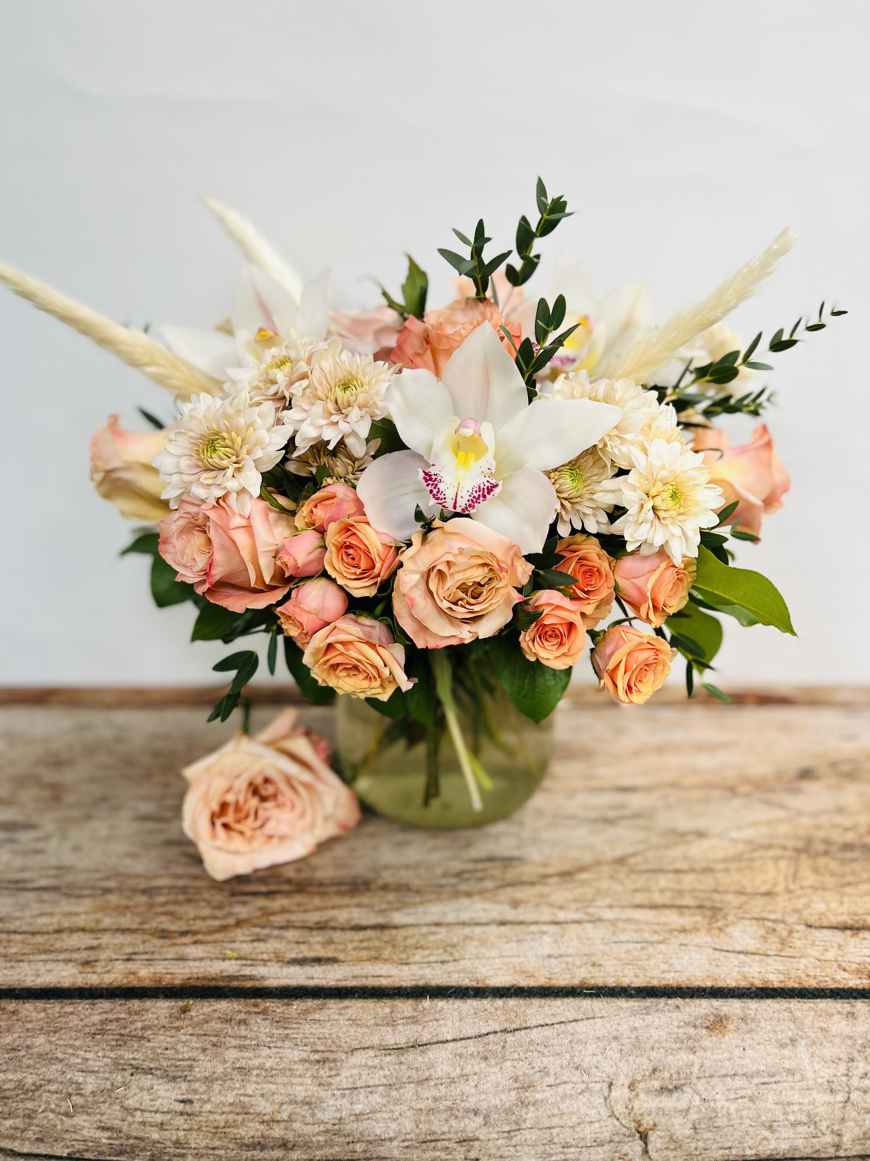 Peach roses and white orchid bouquet in a glass vase