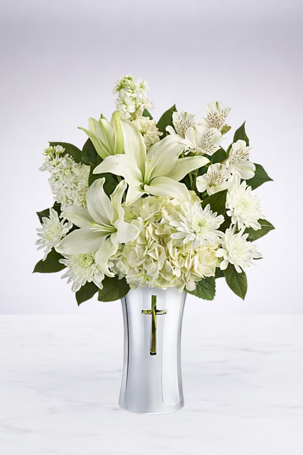 Heavenly White Remembrance  - A beautiful all-white sympathy arrangement featuring elegant lilies, hydrangeas, and seasonal white blooms, designed in a keepsake vase with a silver cross. This peaceful arrangement is a thoughtful way to express love, sympathy, and remembrance during difficult times.