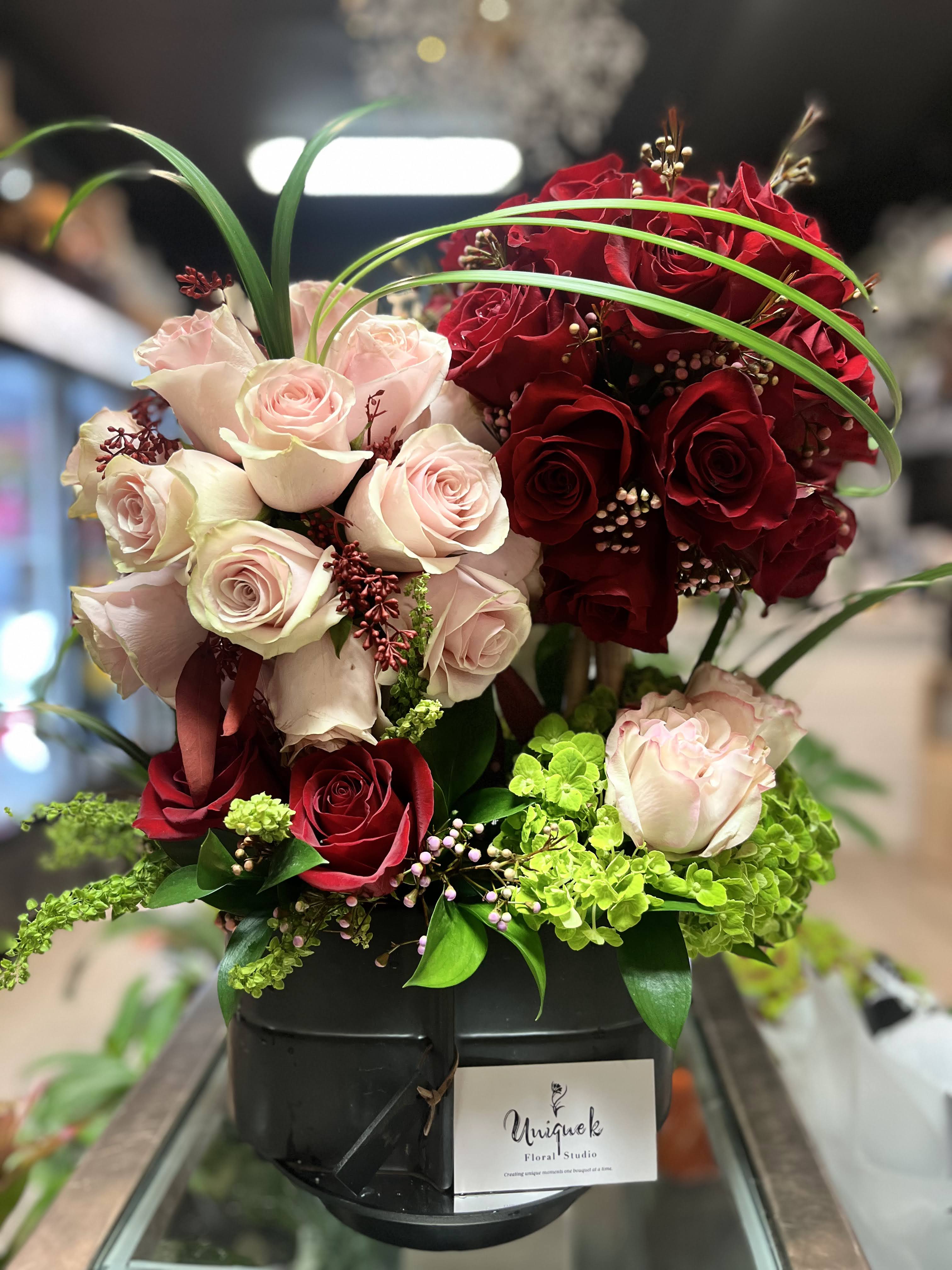 Red and pale pink roses arranged in a black vase with green accents.